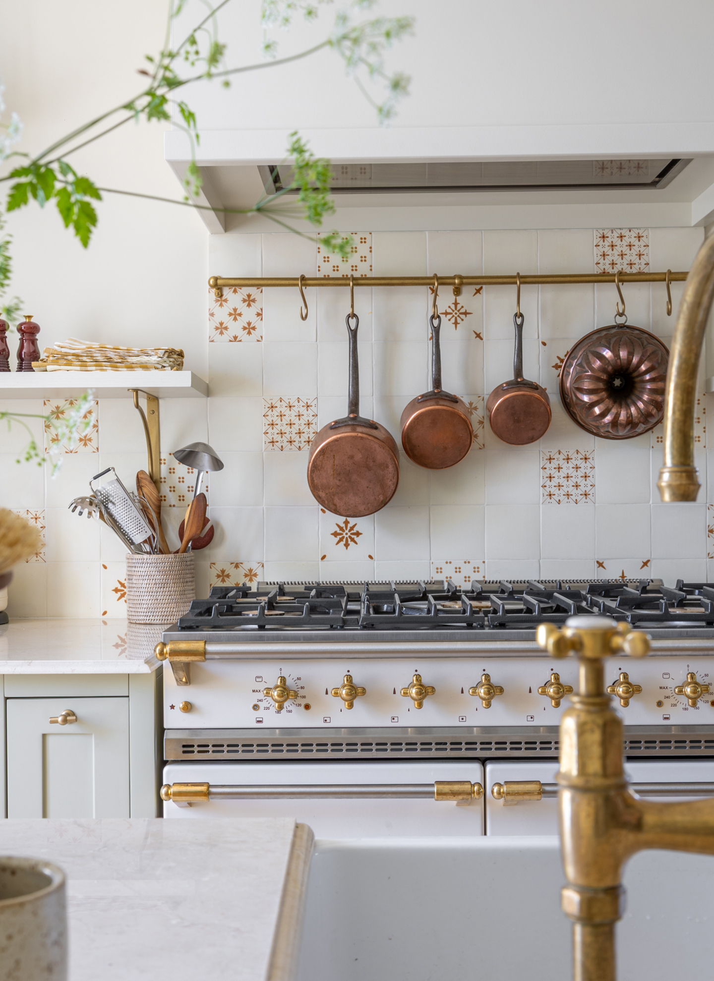 a kitchen with a large white range cooker with copper utensils hanging above it and white and brown patterned tiles