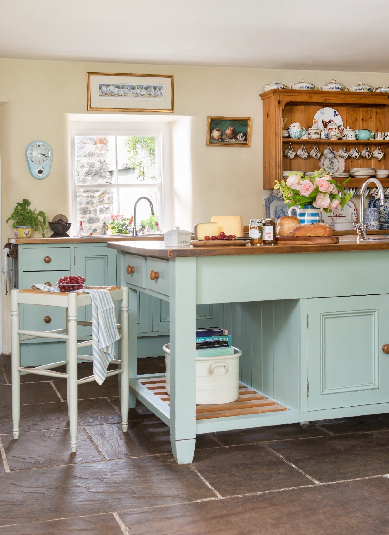 a cottage kitchen with stone flooring, a large kitchen island and cabinetry painted in pale blue