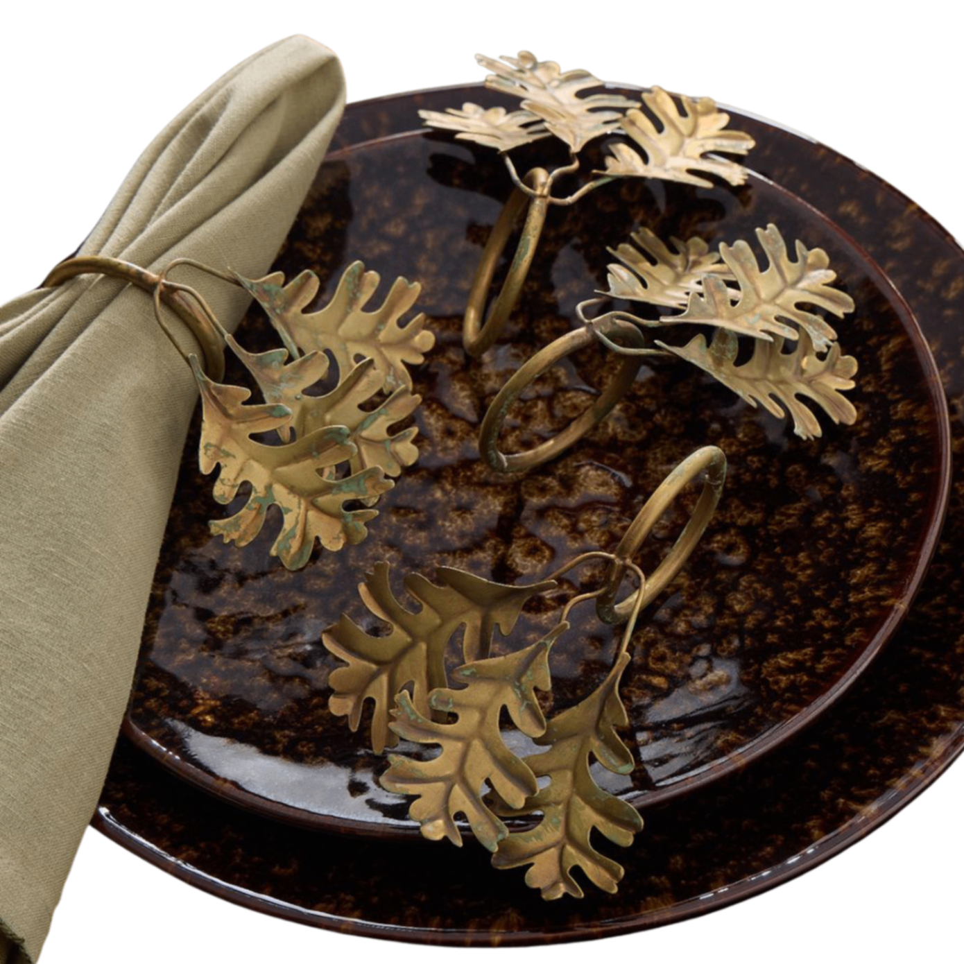 a set of 4 gold leaf shape metal napkin rings on a brown plate with a beige napkin