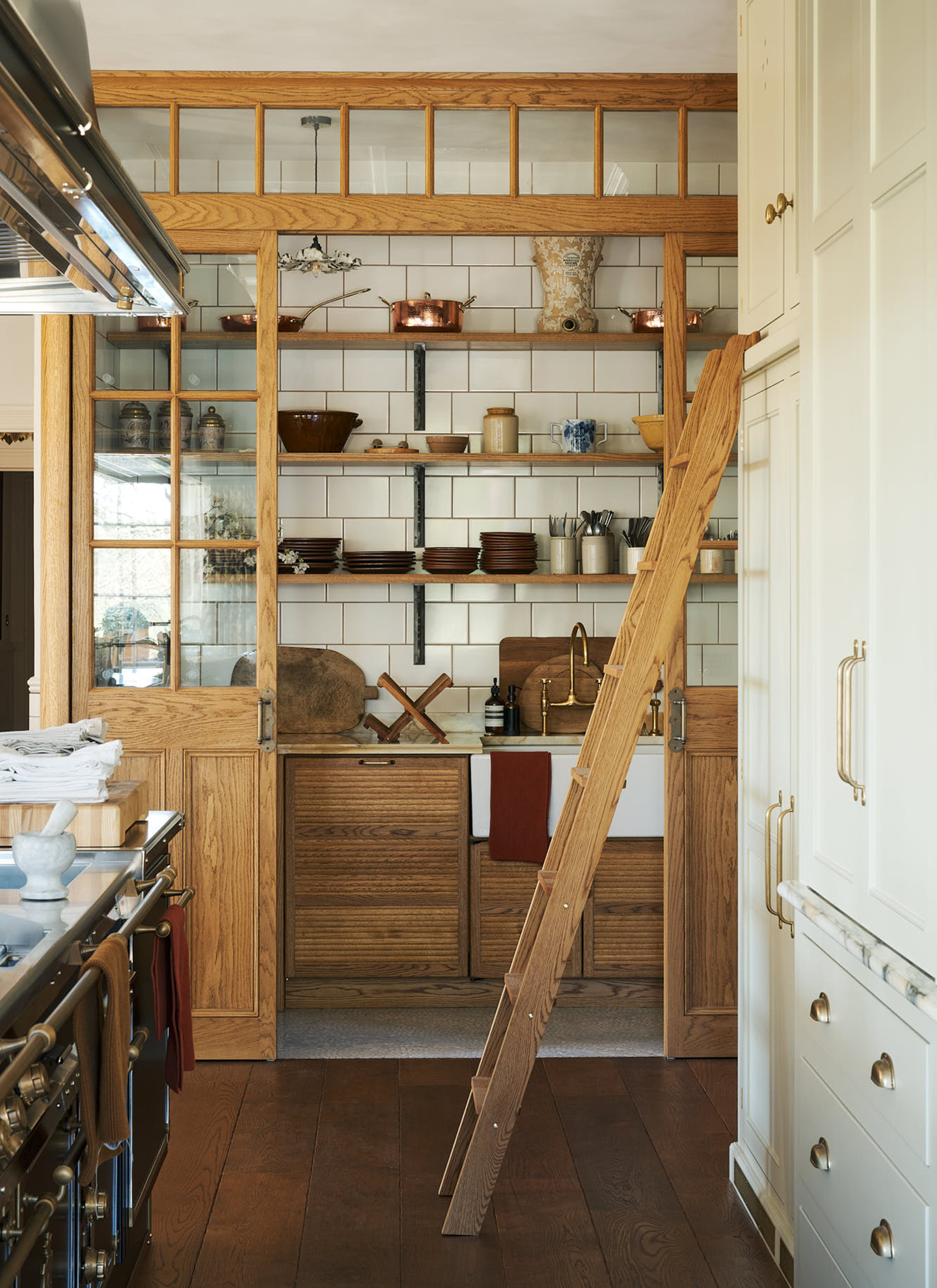 a kitchen with a black range cooker, white cabinetry with a wooden library ladder and wooden doors leading to a pantry