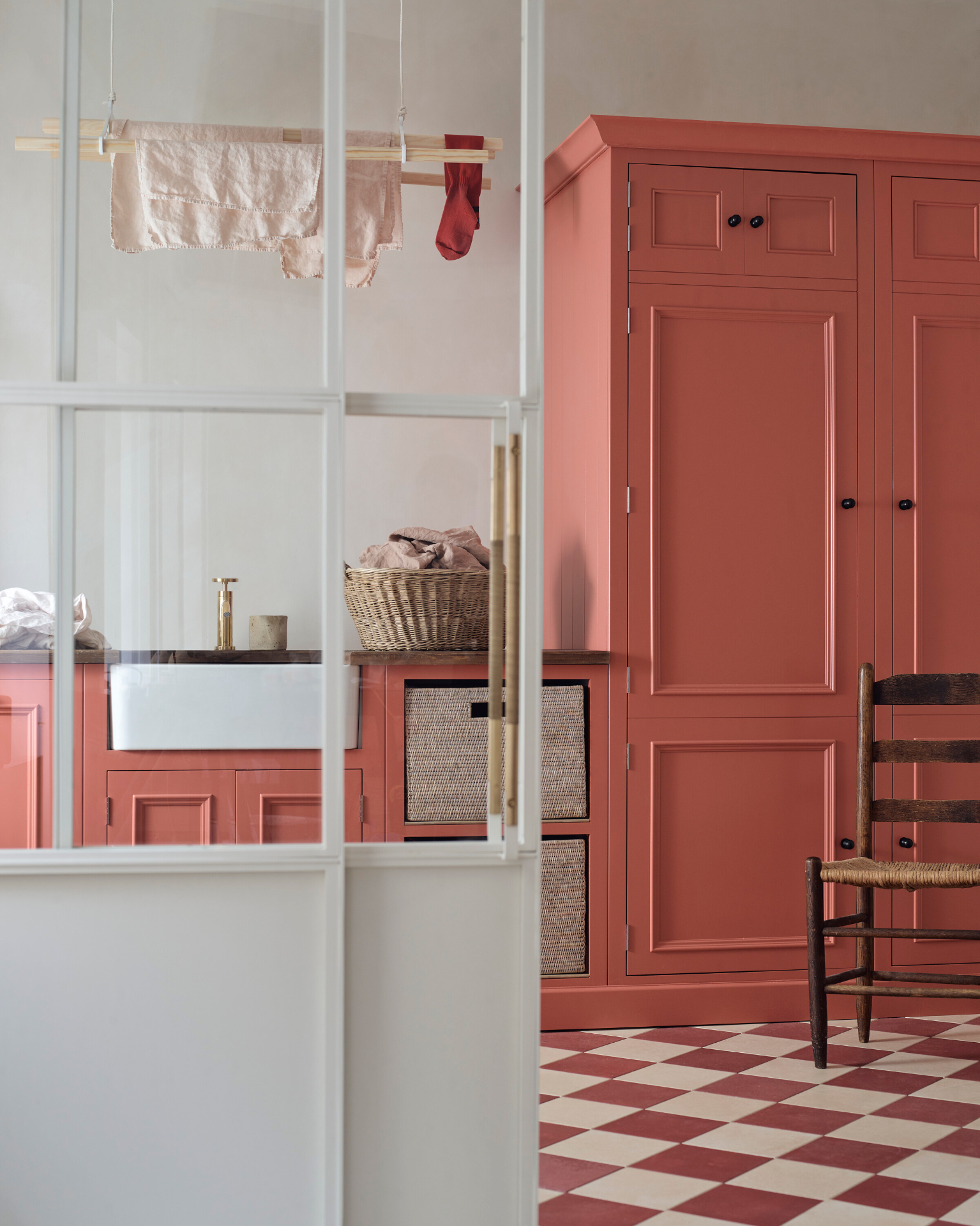 a utility room with coral pink cabinets, red and white checkered floor tiles and a wooden hanging clothes airer
