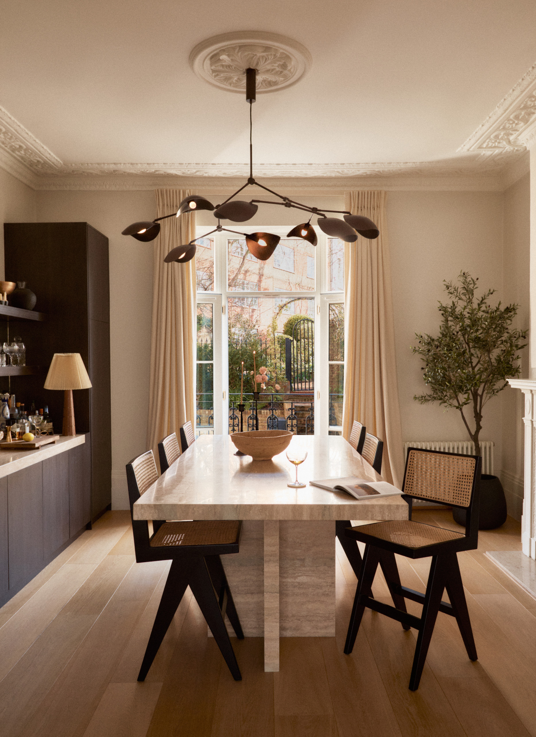 Elegant modern dining room with a stone table, woven cane back chairs, beige drapes, and a sculptural black branch pendant light