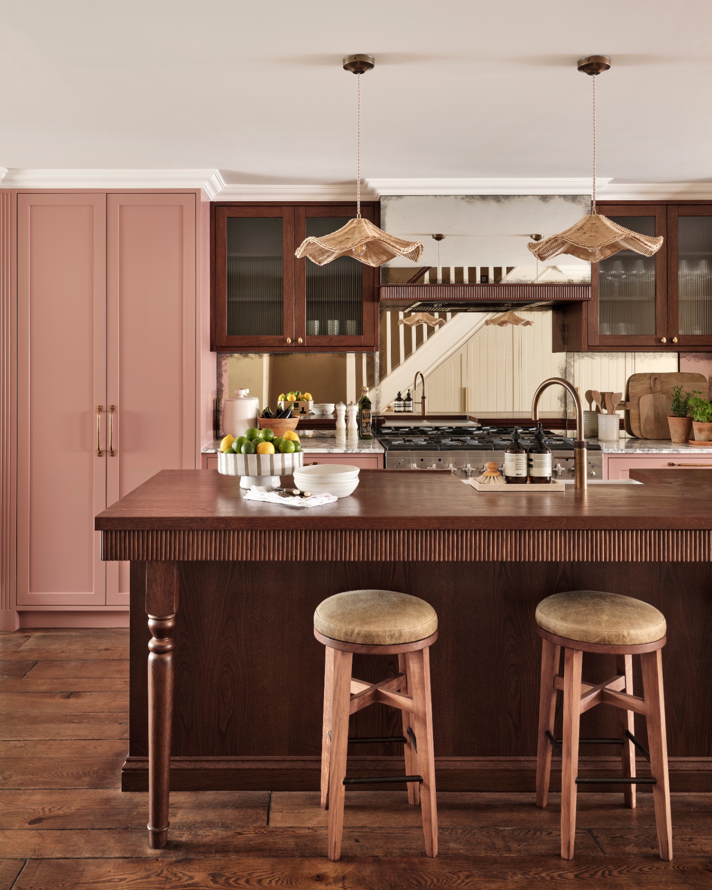 a kitchen with pink and dark wood kitchen cabinets, a dark wood kitchen island with two stools tucked under it and two large rattan pendant shades hanging above it