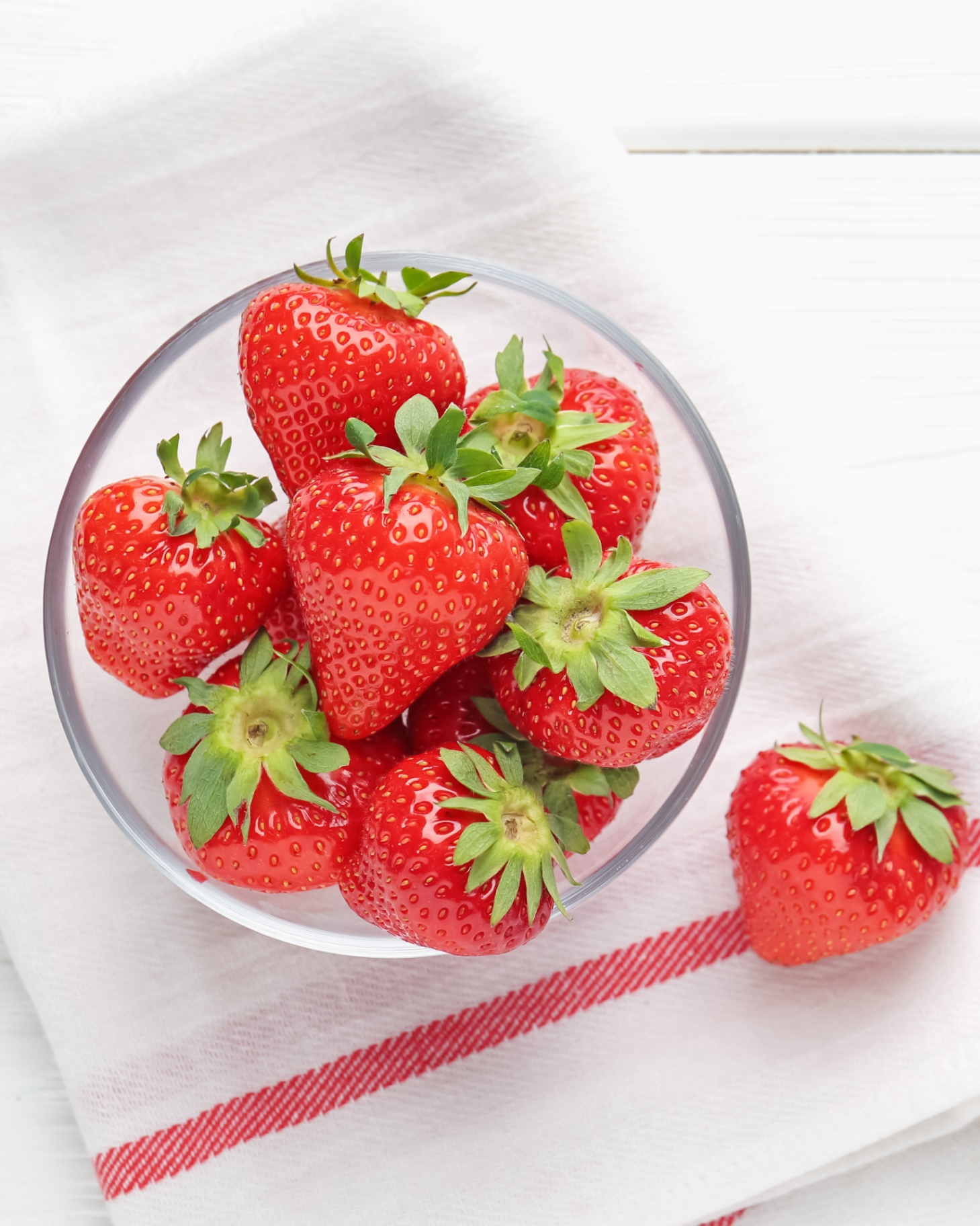a glass bowl of fresh strawberries on a white and red stripe tea towel