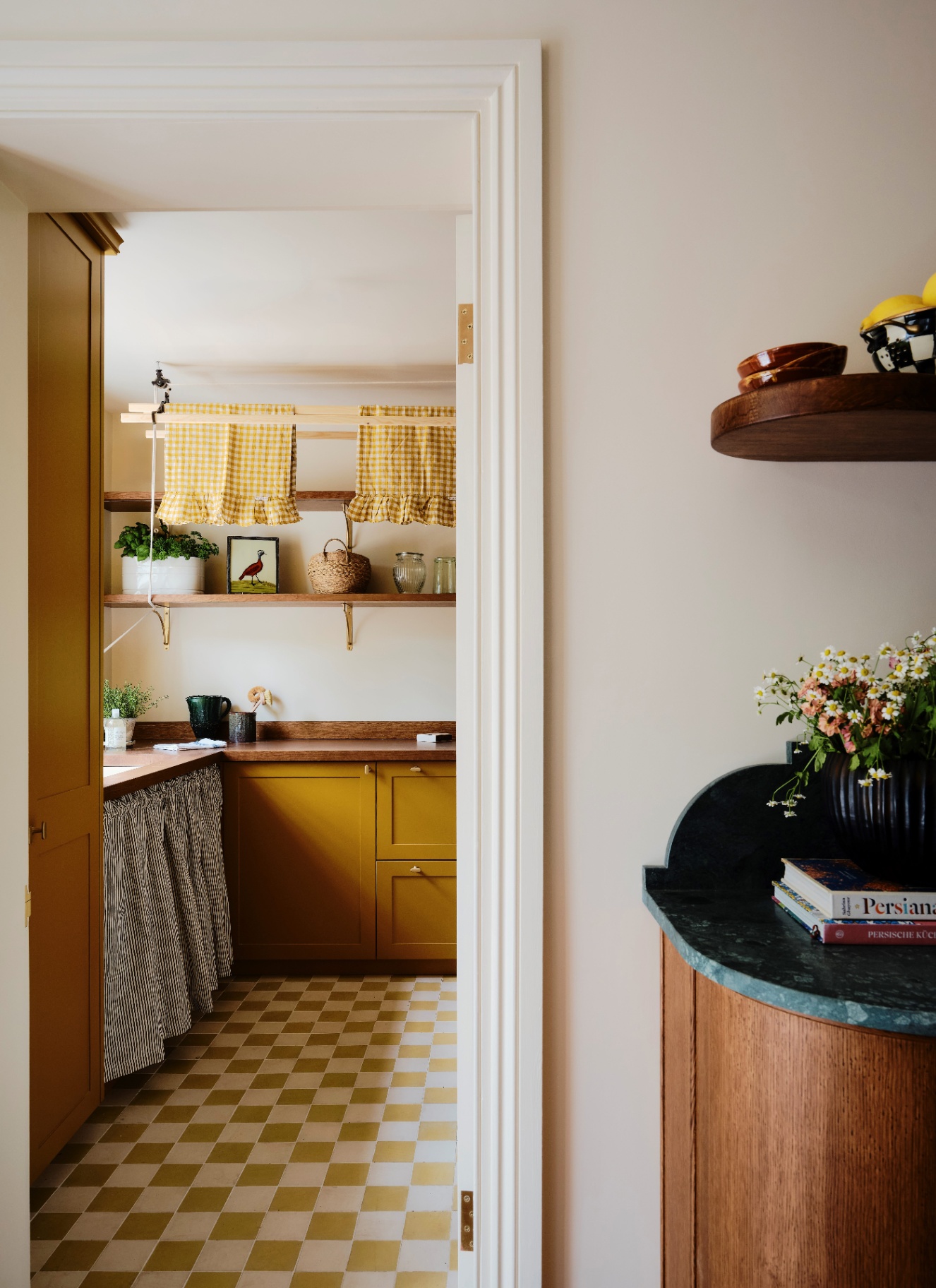 an open door looking into a utility room with yellow and which checkerboard flooring, mustard cabinets, wooden countertops and wooden open shelves