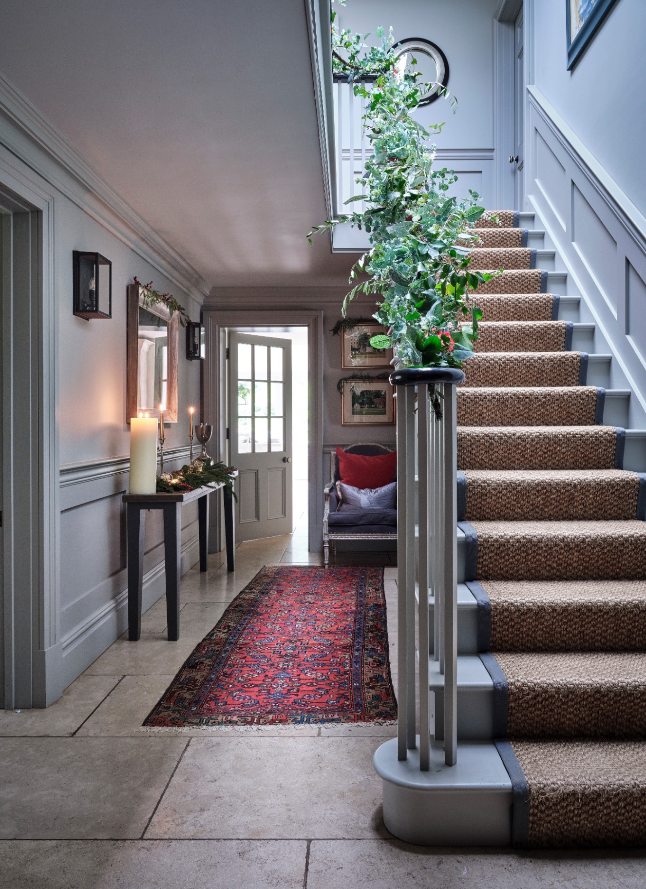 A grand hallway staircase banister wrapped in a cascading garland of trailing eucalyptus, ivy, and red berries.