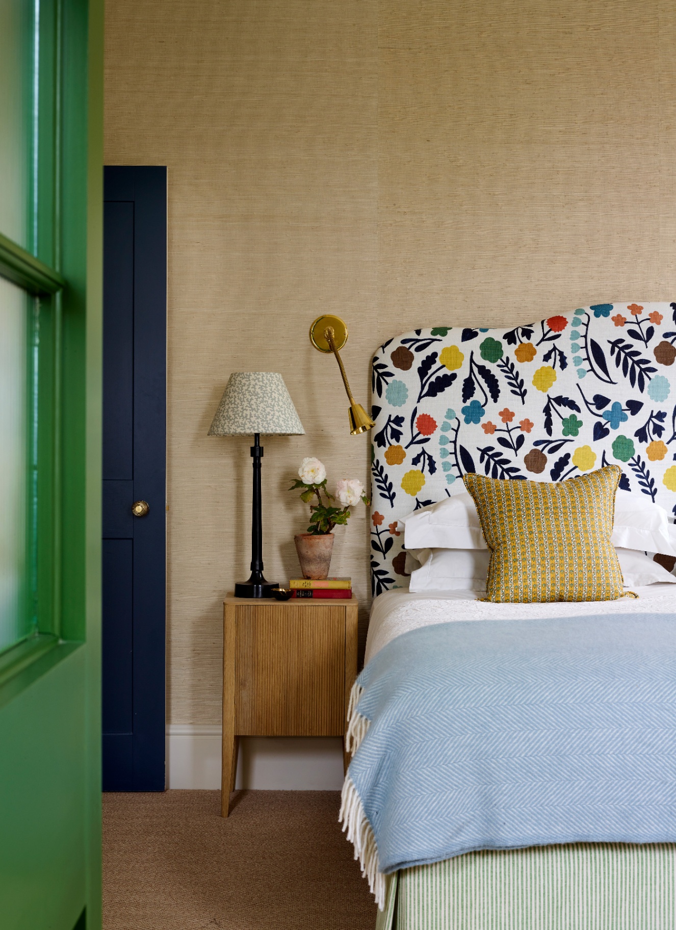 A colorful bedroom featuring an adjustable brass wall sconce with a small shade mounted above a floral upholstered headboard