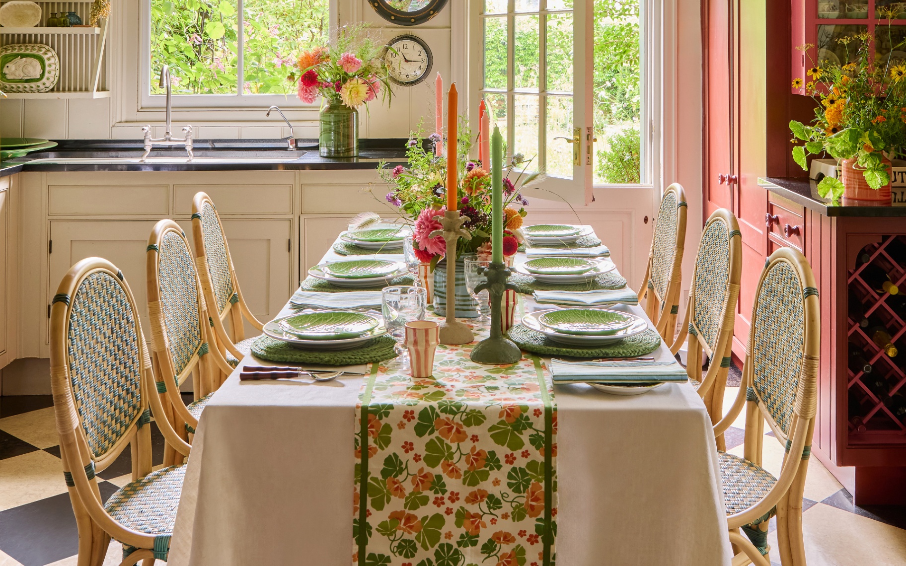a kitchen diner with a long table covered in a white cloth and a green patterned runner, green bistro chairs, green and pink dinner candles and colourful flowers in vases
