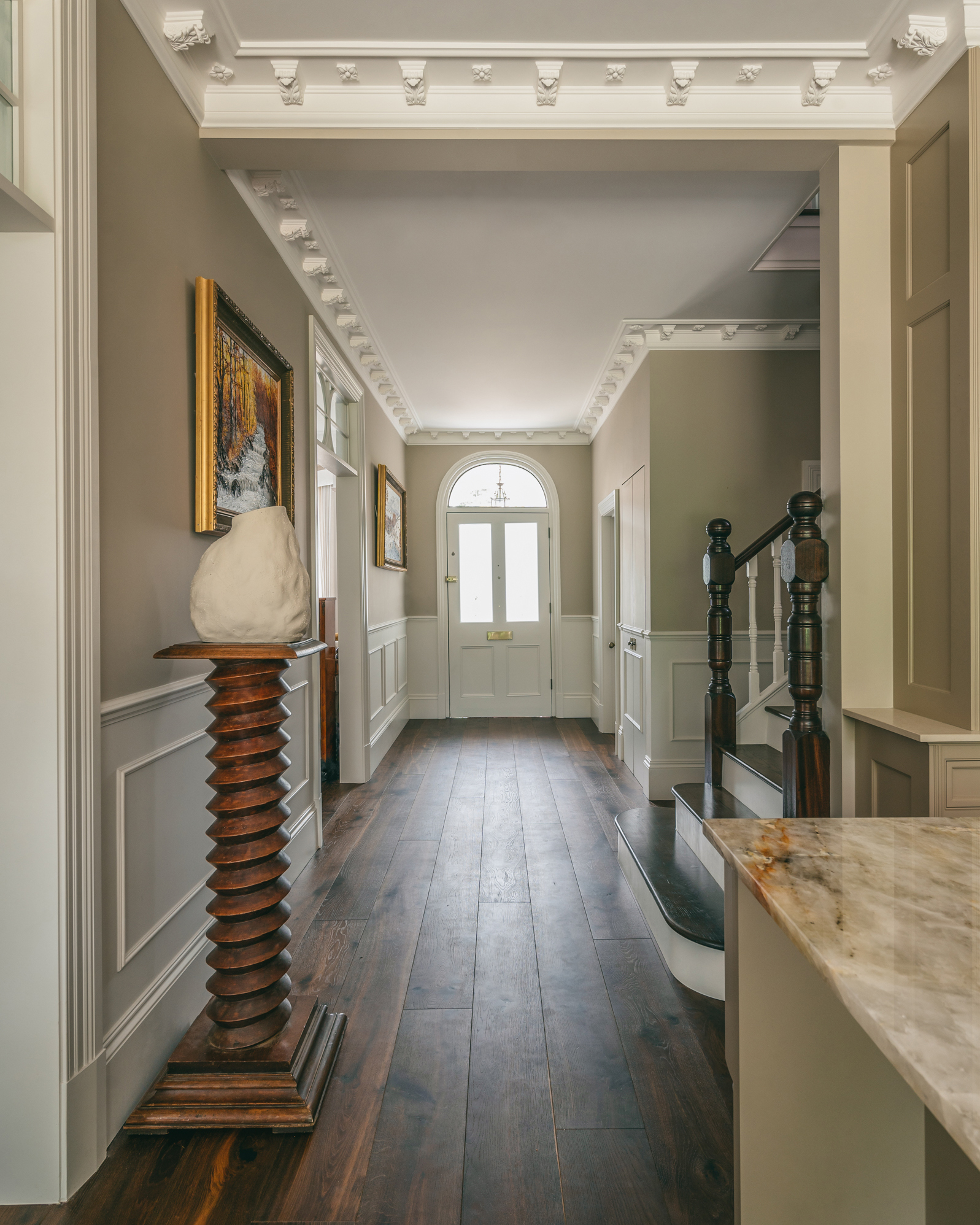 a large grand hallway with white and neutral paneled walls and dark wood floor