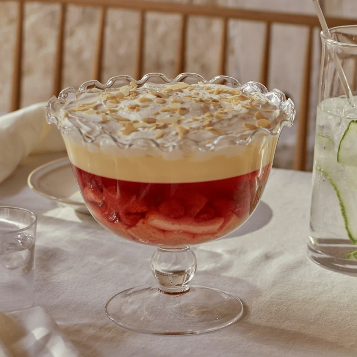 a clear glass trifle bowl with a wavy edge, with a trifle inside on a white tablecloth