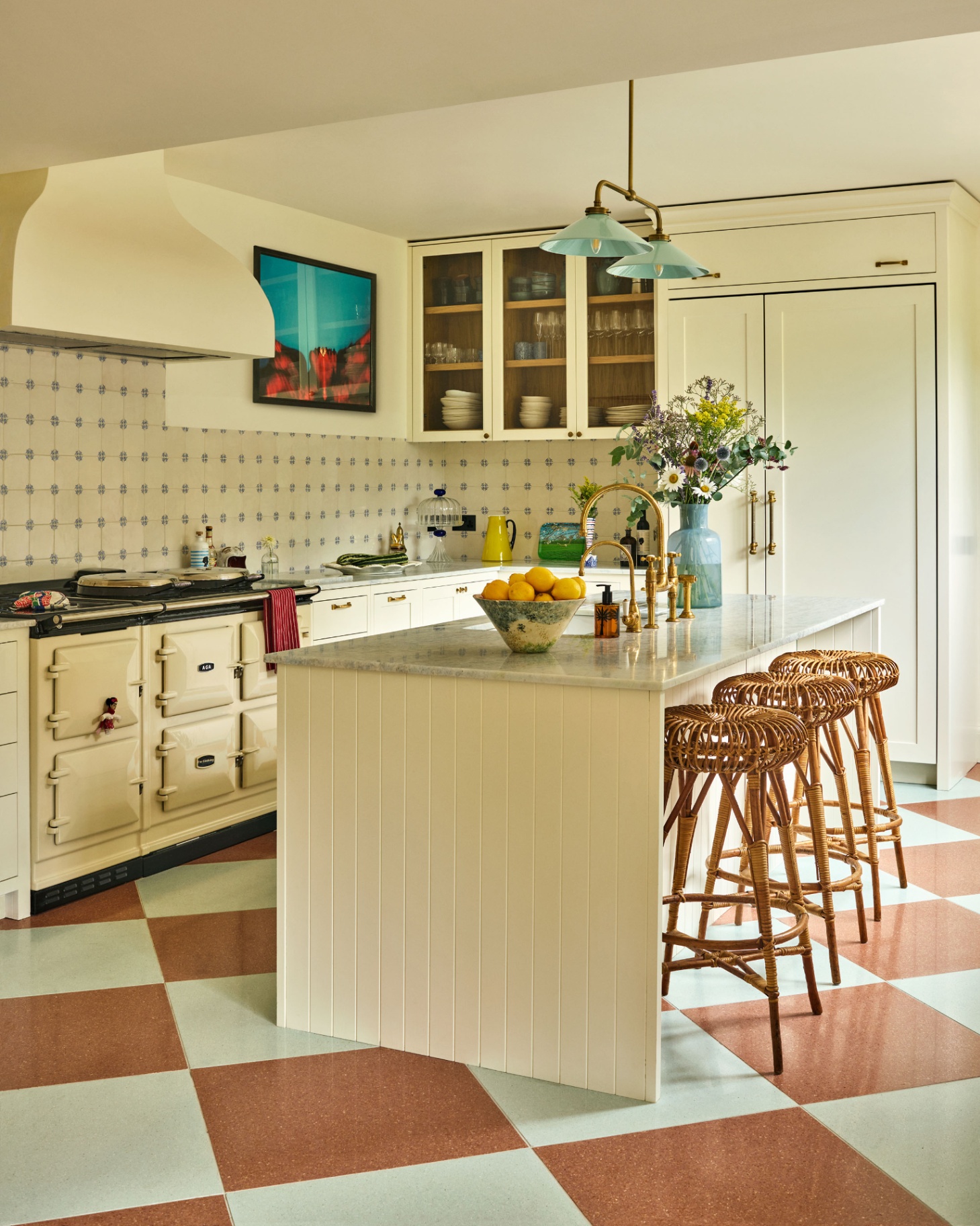 a kitchen with a white and orange checkerboard floor, a white and marble kitchen island with rattan stools and a cream aga