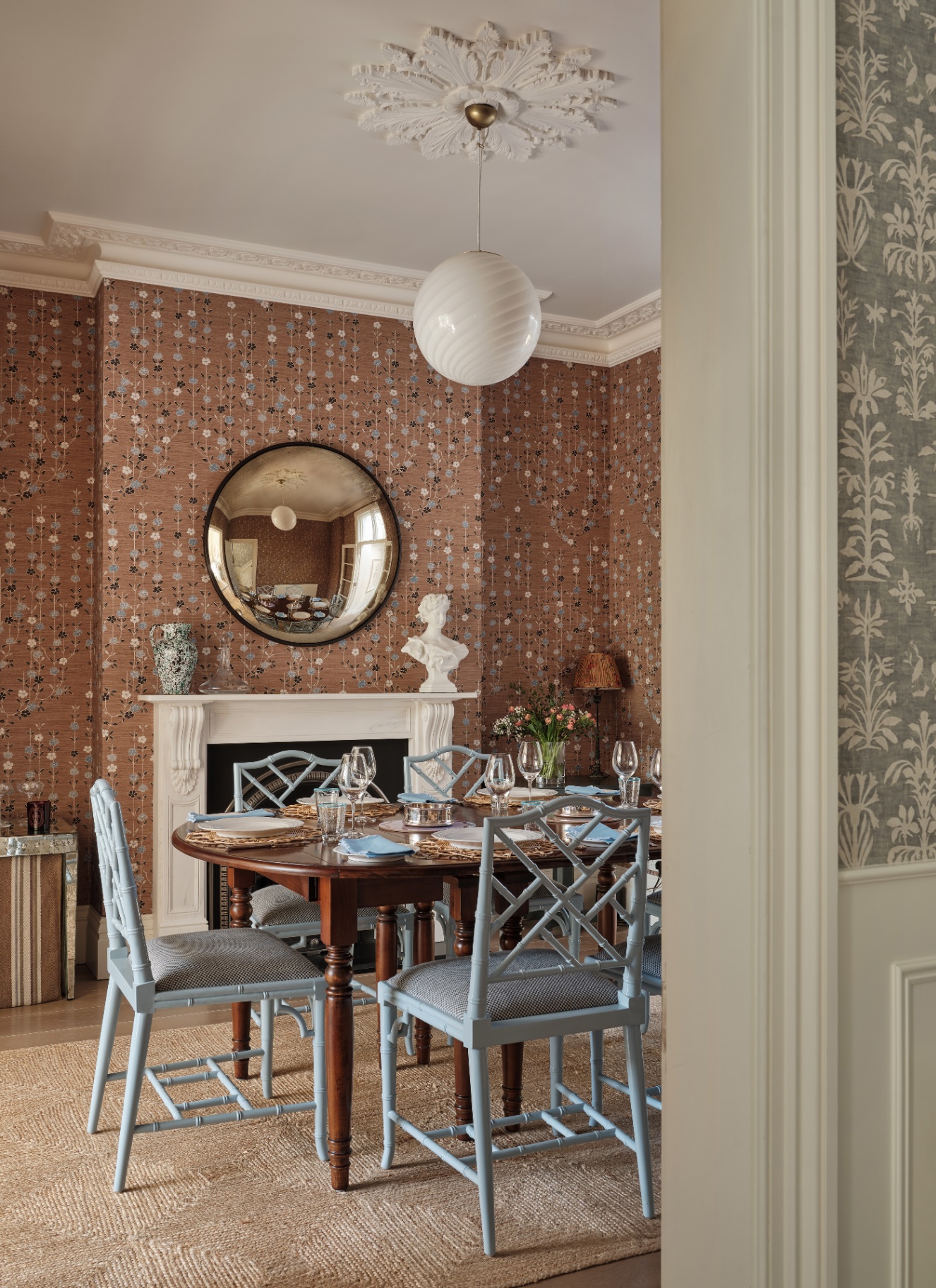 Dining room with patterned brown wallpaper, light blue dining chairs around a dark wood table, and a white globe pendant.