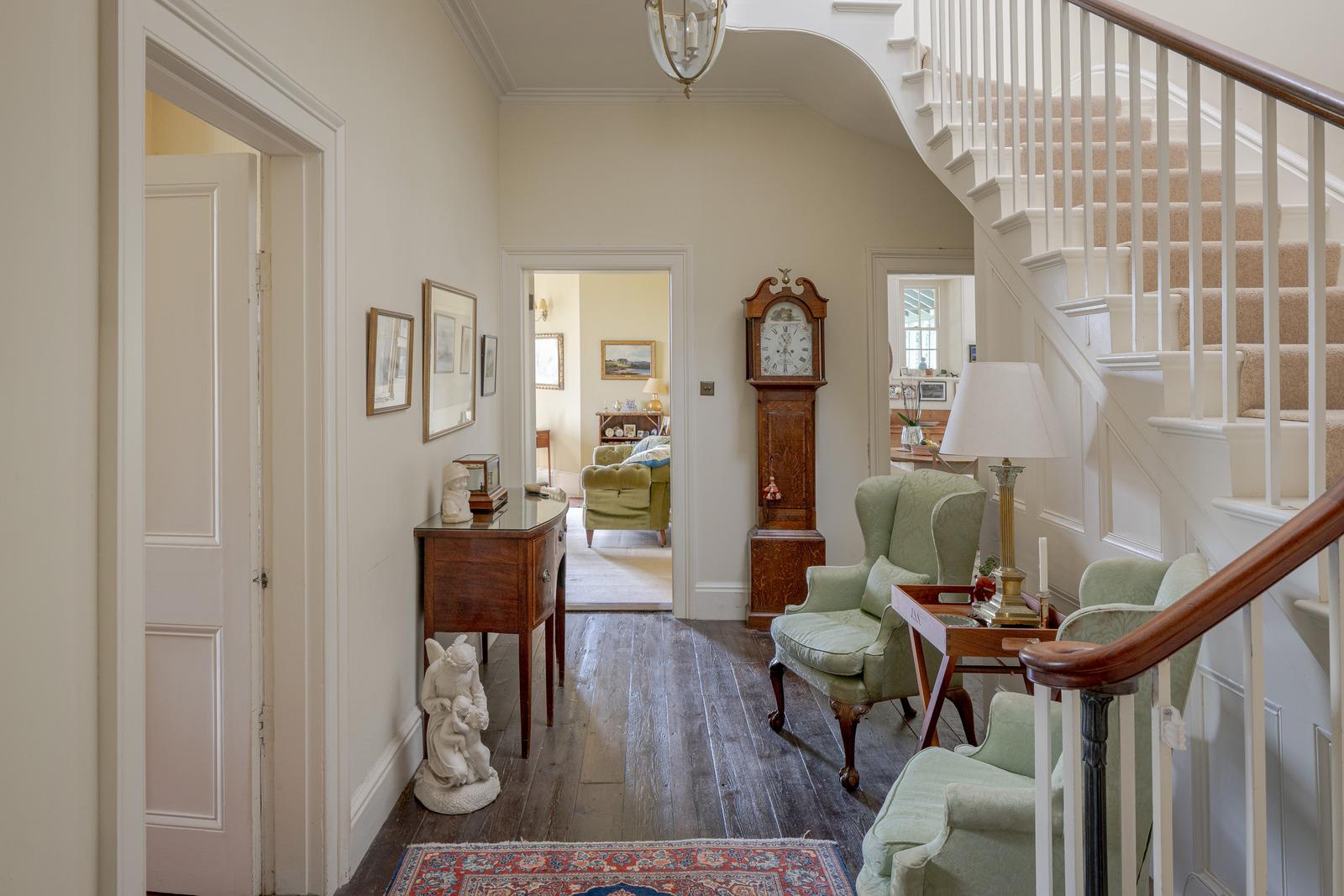 a hallway with white walls, wooden floors, a sweeping staircase and a grandfather clock