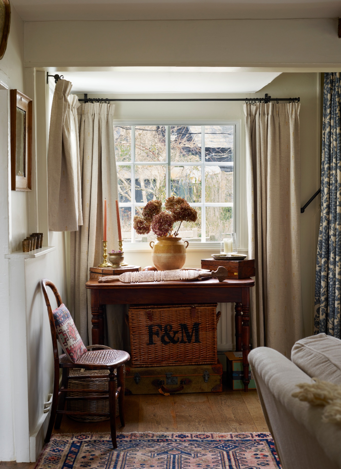 a living room corner with a wooden table, a wicker basket under it, a vase wtih dried hydrangeas and a small wooden dining chair