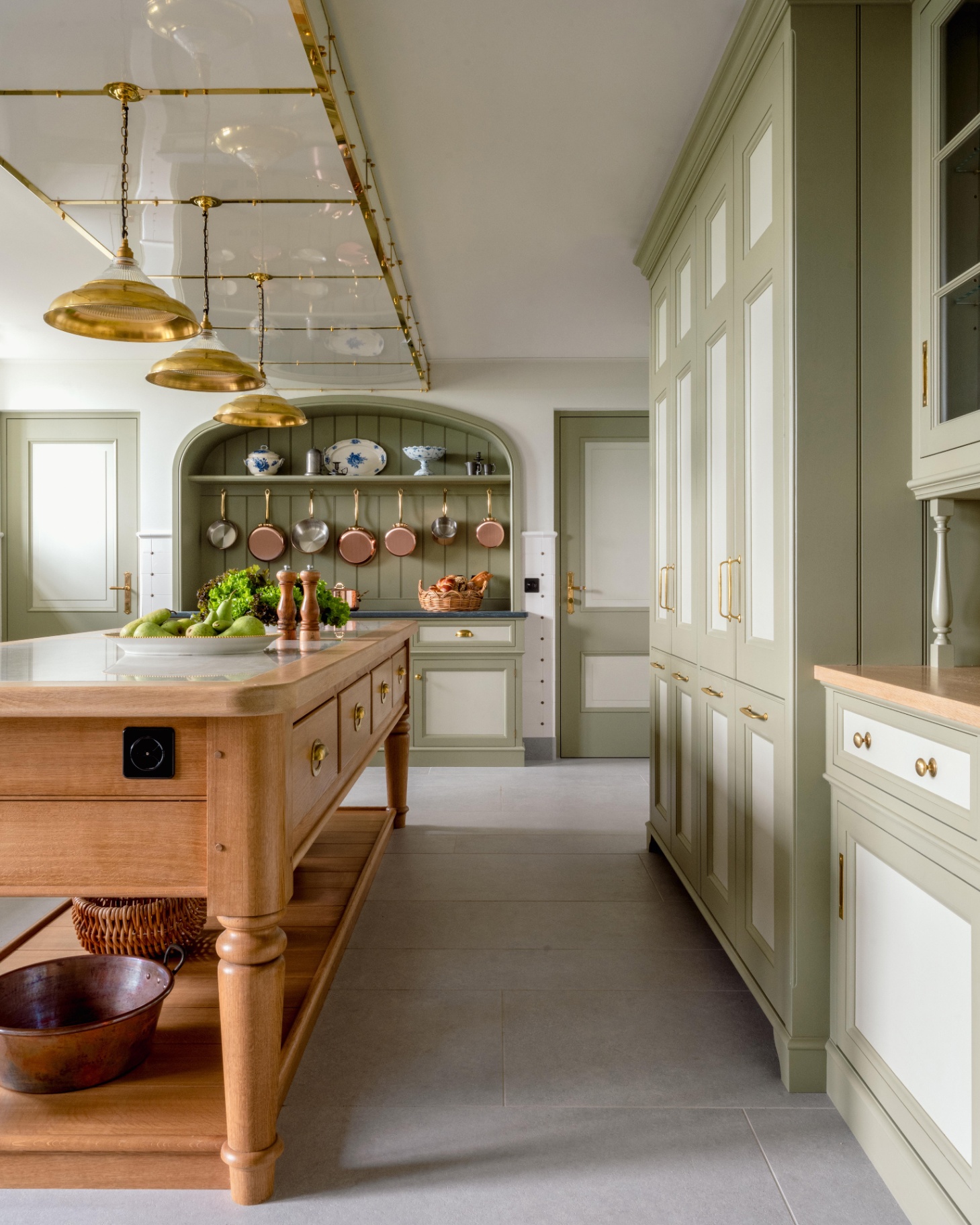 a kitchen with sage green cabinetry, a large wooden butchers block with 3 gold pendant lights hanging above it