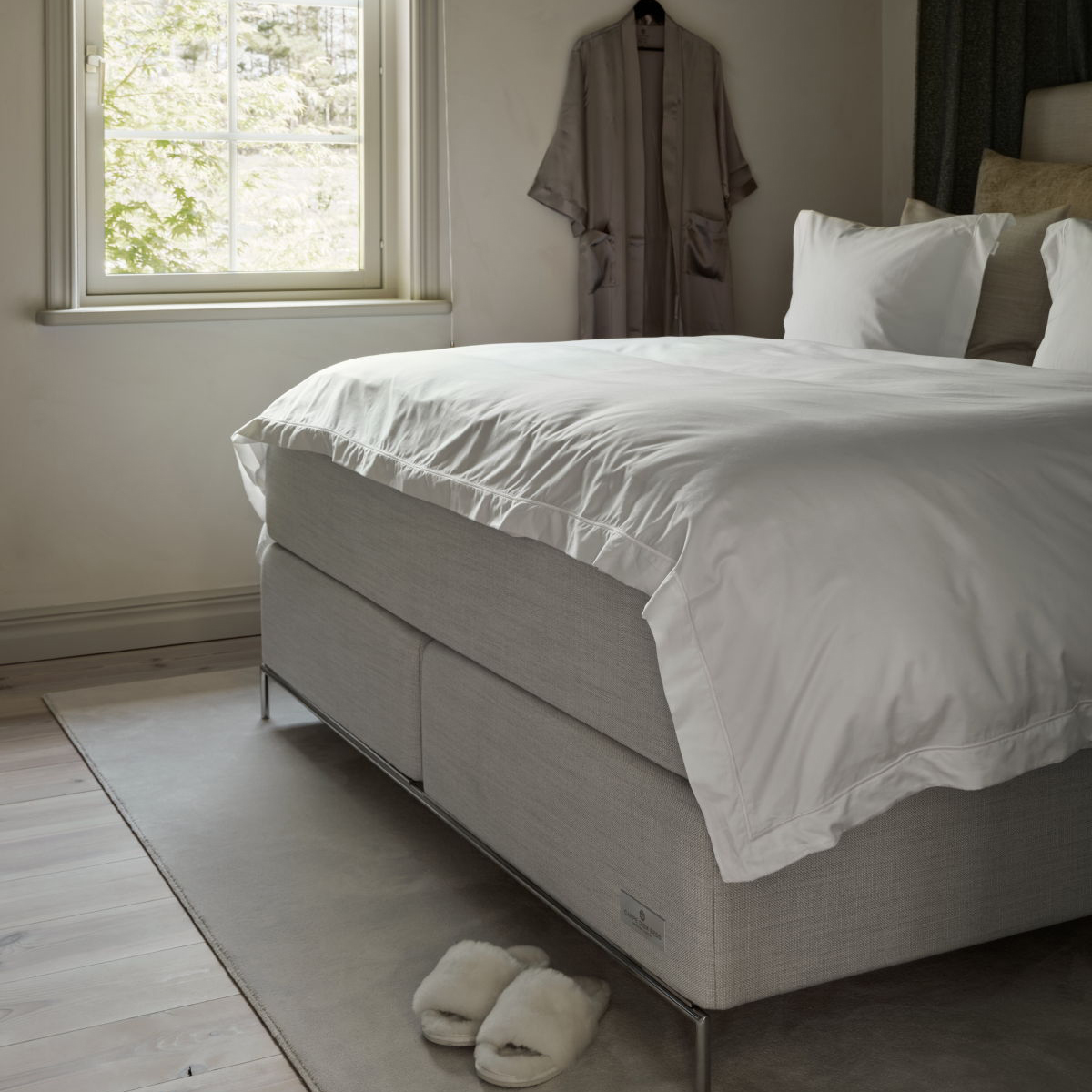 carpe diem bed with a silk robe hung up on the wall and fluffy slipper on the floor