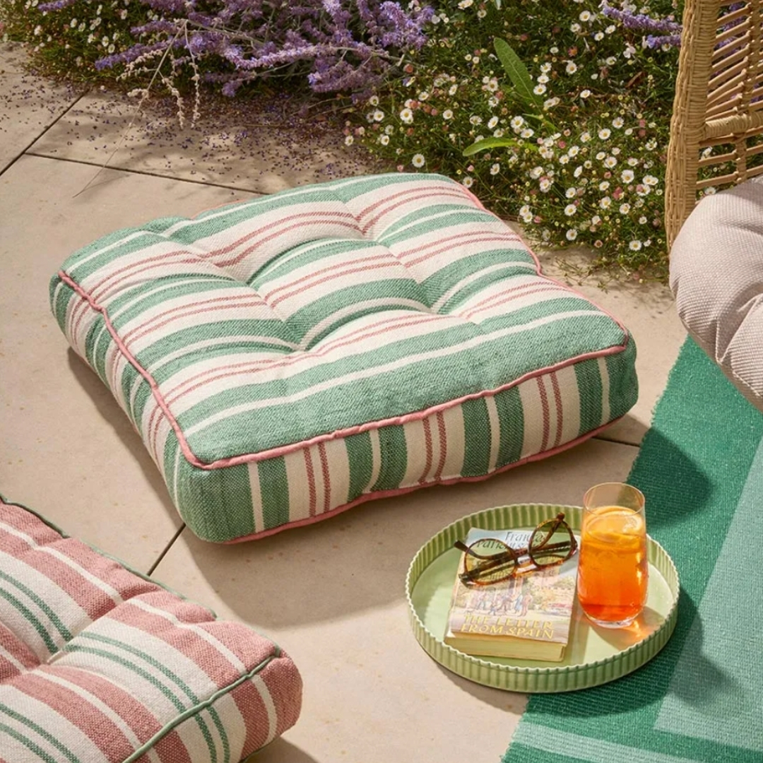 Cox and Cox outdoor floor cushion pictured outside in a garden with a glass of aperol