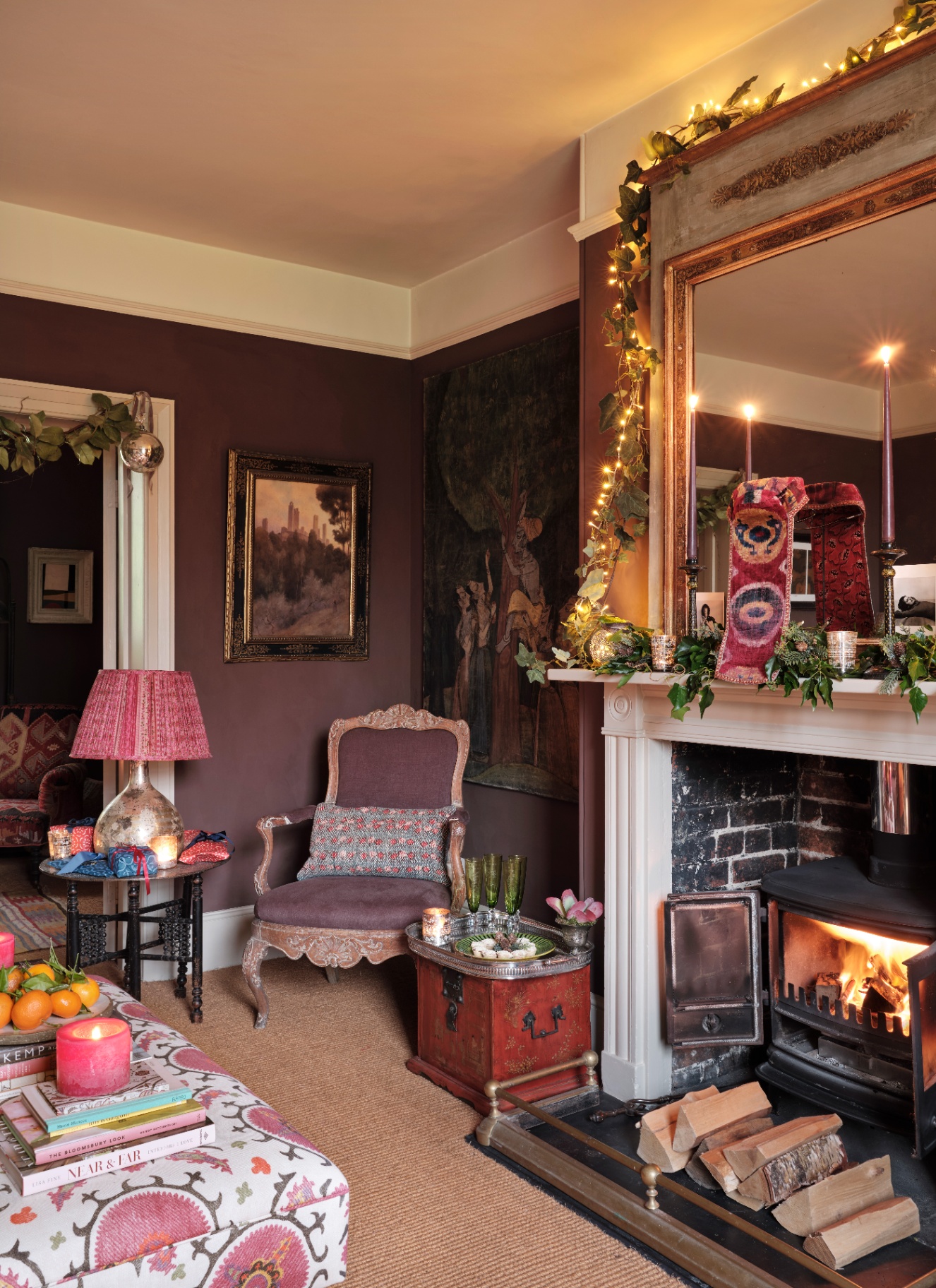 A moody plum-colored sitting room with a fairy-lit ivy garland draped around an ornate fireplace mirror