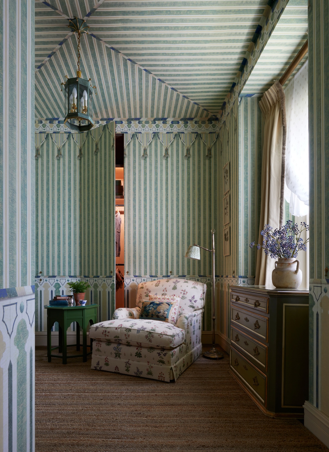 a sitting room with all over white and green striped walls and ceiling, a jib door and a cream floral armchair