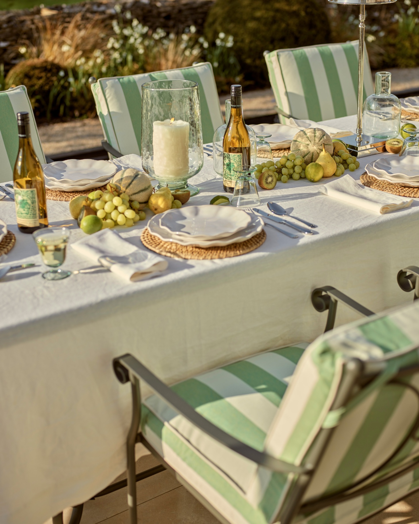 an outdoor dining table with chairs with white and green stripe seat cushions, ruffle edge plates and fresh fruit in the centre