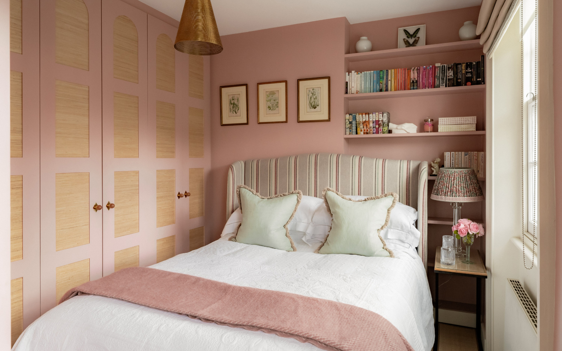 ttan panelled doors, a double bed with a grey and pink stripe headboard and white bedding and a built in bookcase above the bed filled with colourful books