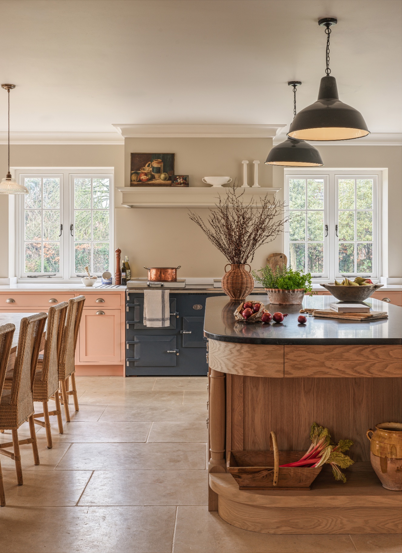 a kitchen with stone flooring, a large wooden kitchen island with a black top, a dark blue range cooker and pink cabinetry