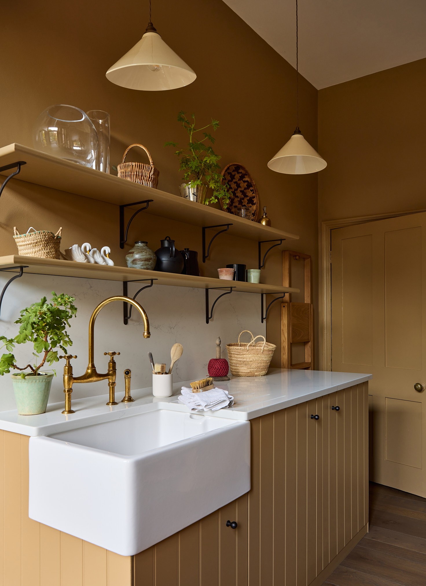 a kitchen with colour drenched mustard yellow cabinets, walls and ceiling, a belfast sink with gold taps and 2 rows of open shelves