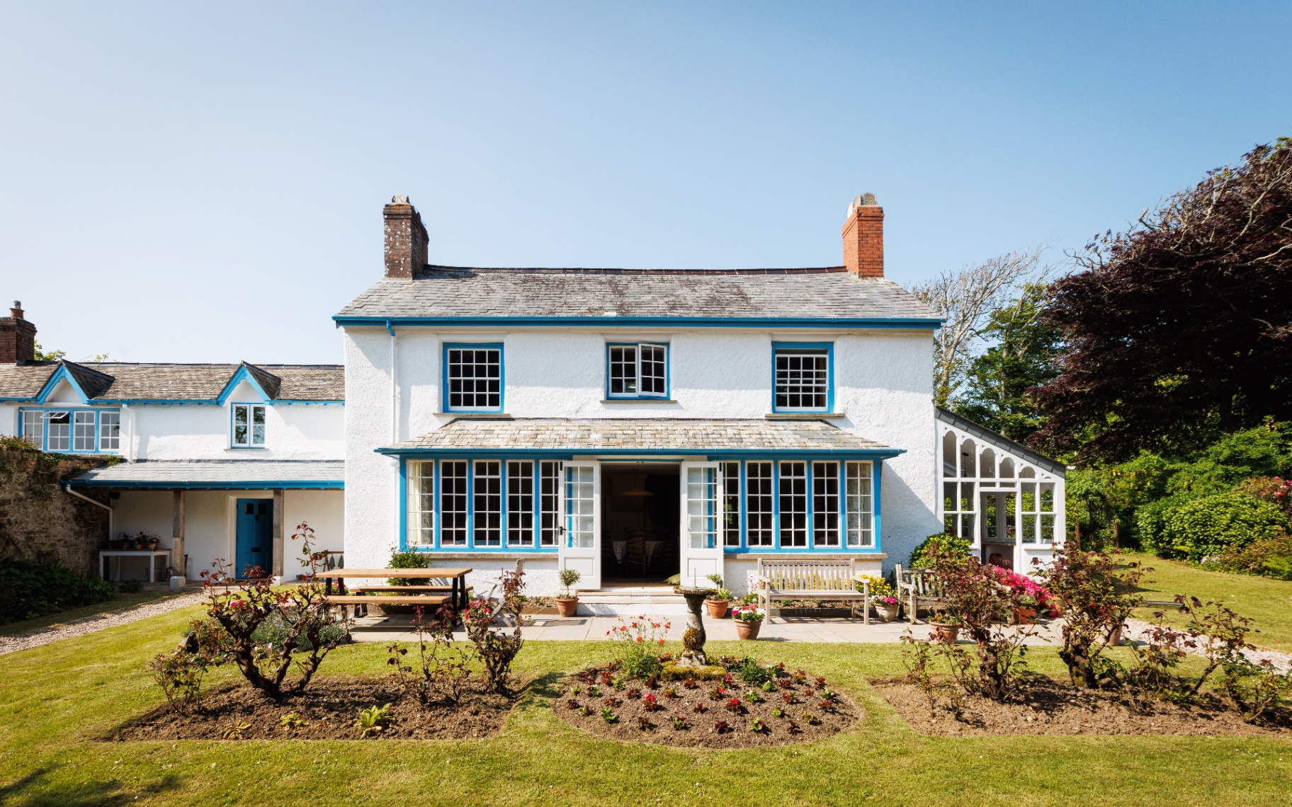 the exterior of a white house with blue windows, blue sky and a lawn