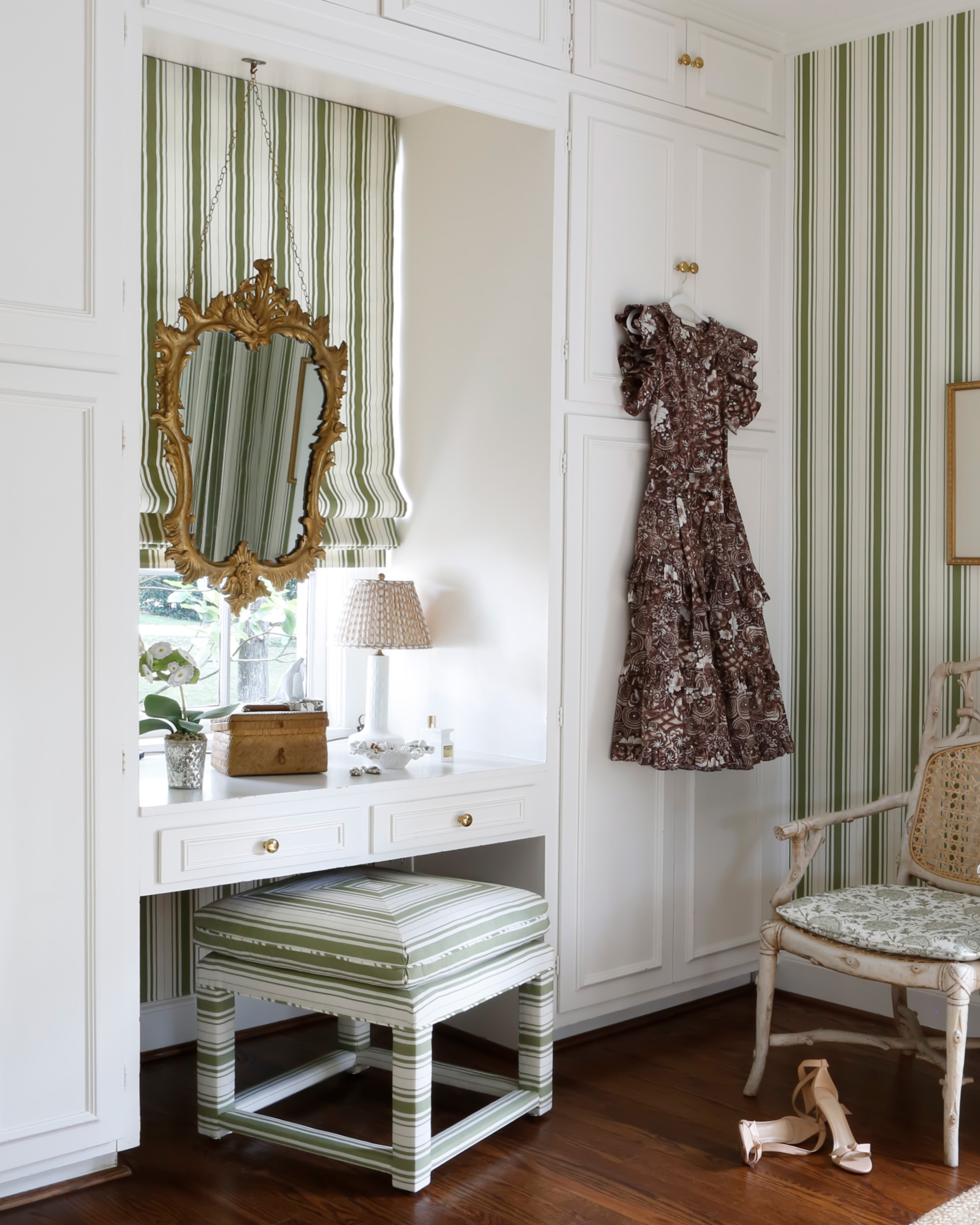 gp j baker and lee jofa green and white stripe fabric and wallpaper in a corner of a dressing room, with a large gold antique mirror above a dressing table anda dress hung on the wardrobe door