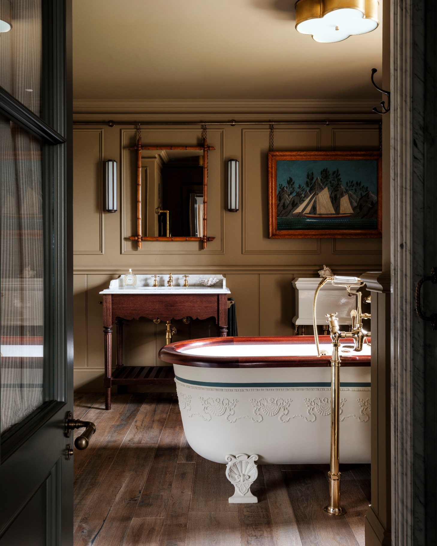 a bathroom with beige panelled walls, a freestanding bath tub with gold hardware, a wooden vanity sink with a large mirror above it
