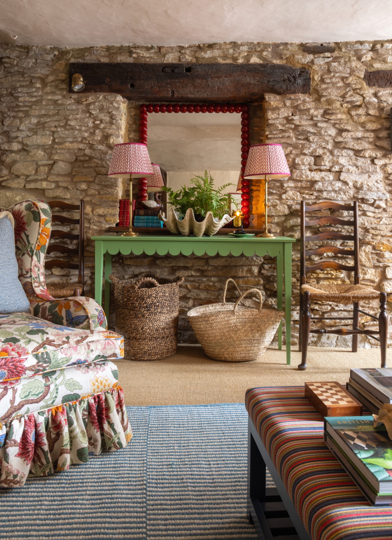 a living room with exposed stone wall, a bright green console table with two pleated lamps and a red bobbin mirror above it