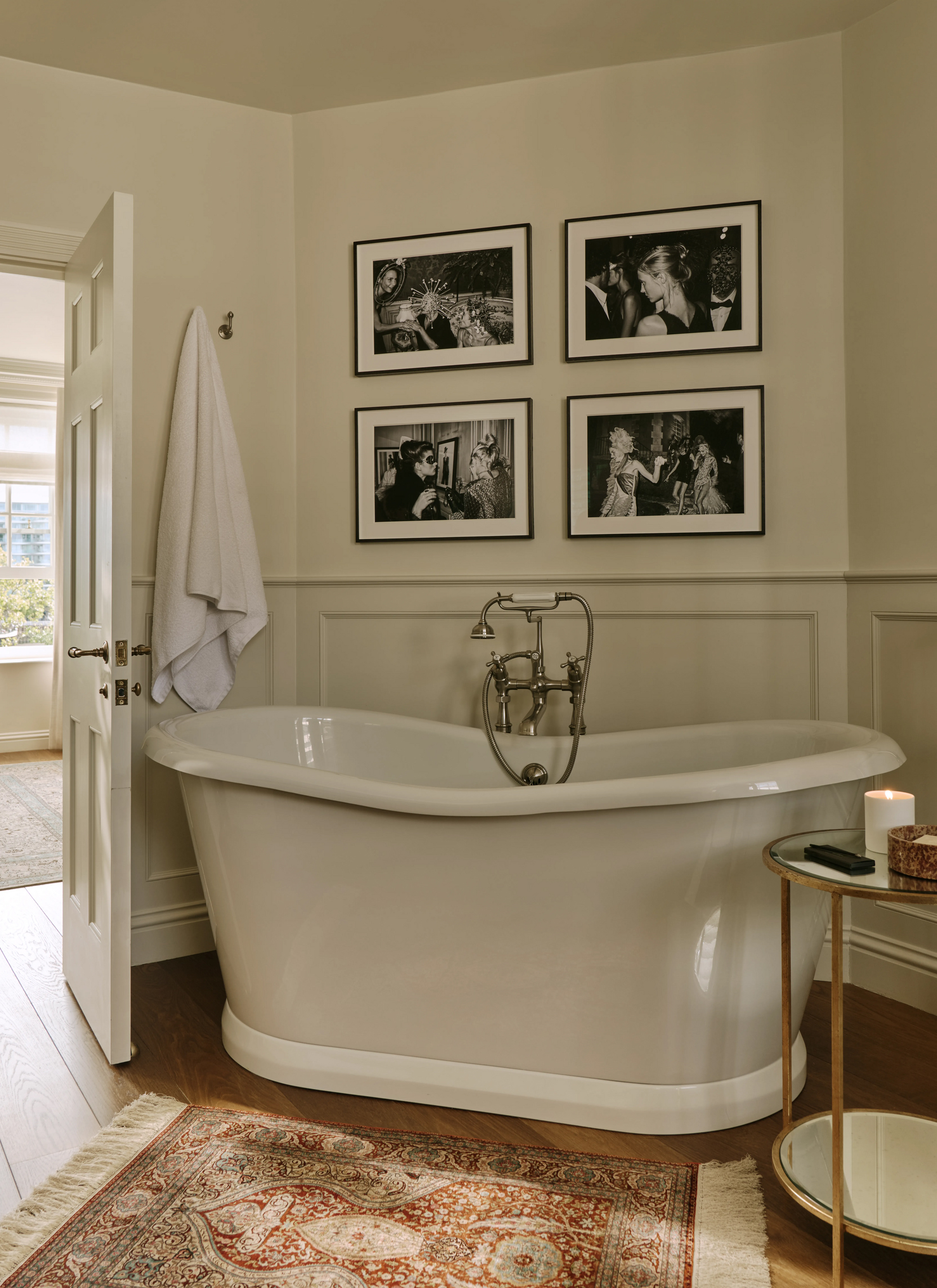 a neutral bathroom with a large freestanding roll top bath tub and a grid of 4 black and white photos in black frames hanging on the wall