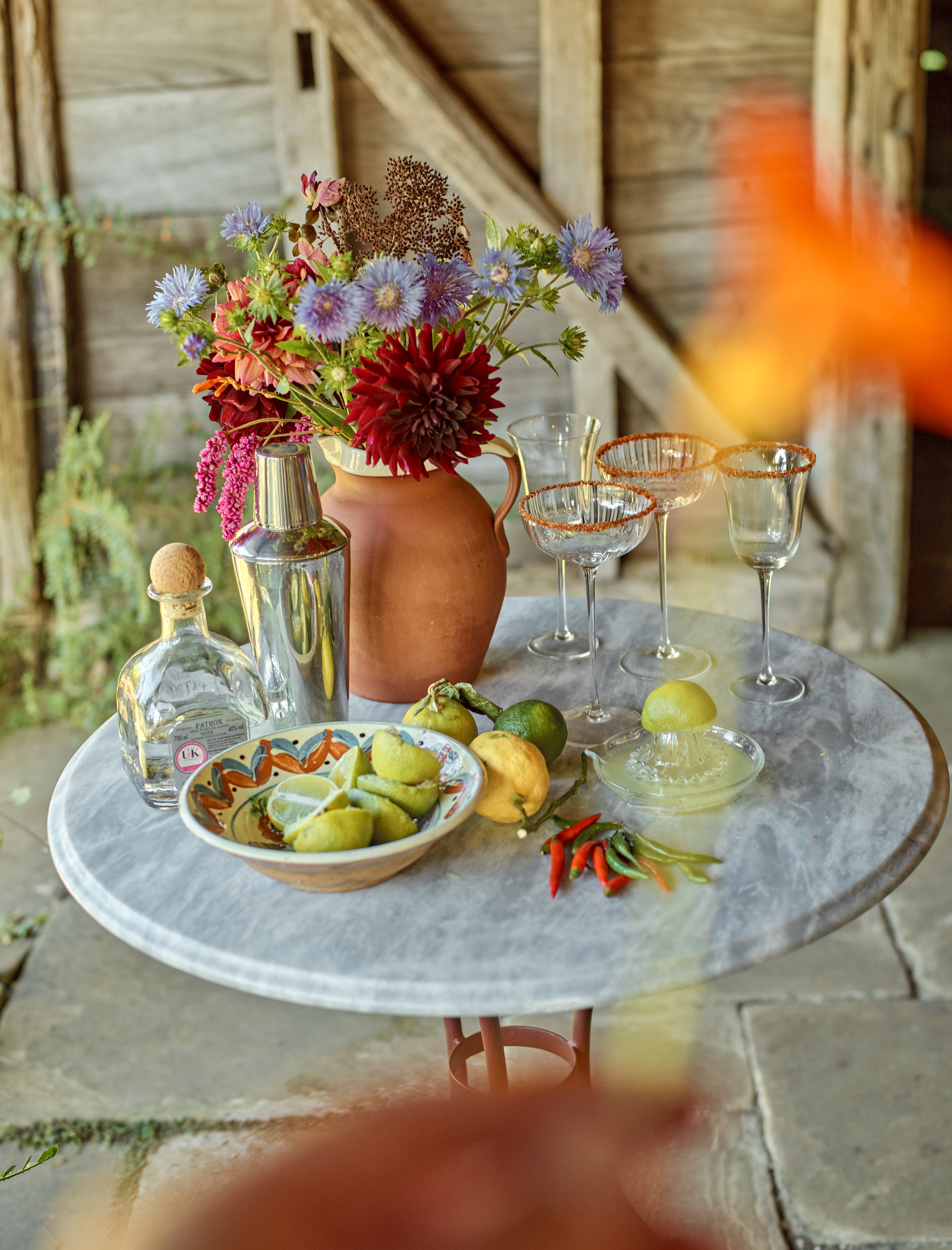 a round marble outdoor table with a large terracotta vase, cocktail glasses and a silver cocktail shaker