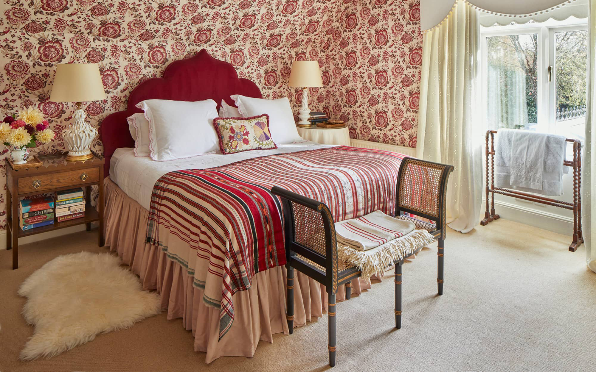 a traditional english bedroom with a large bed with a red headbaord and a red patterned throw