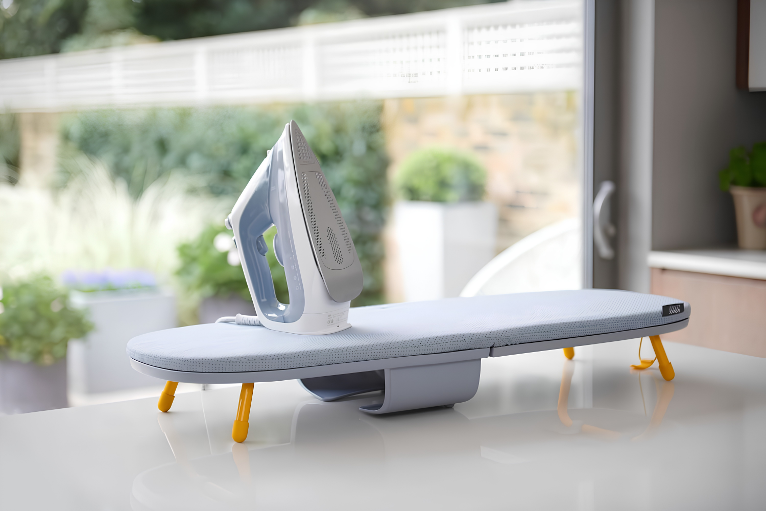 joseph joseph space saving ironing board on a glossy white surface with a white iron on top of it with a garden in the background