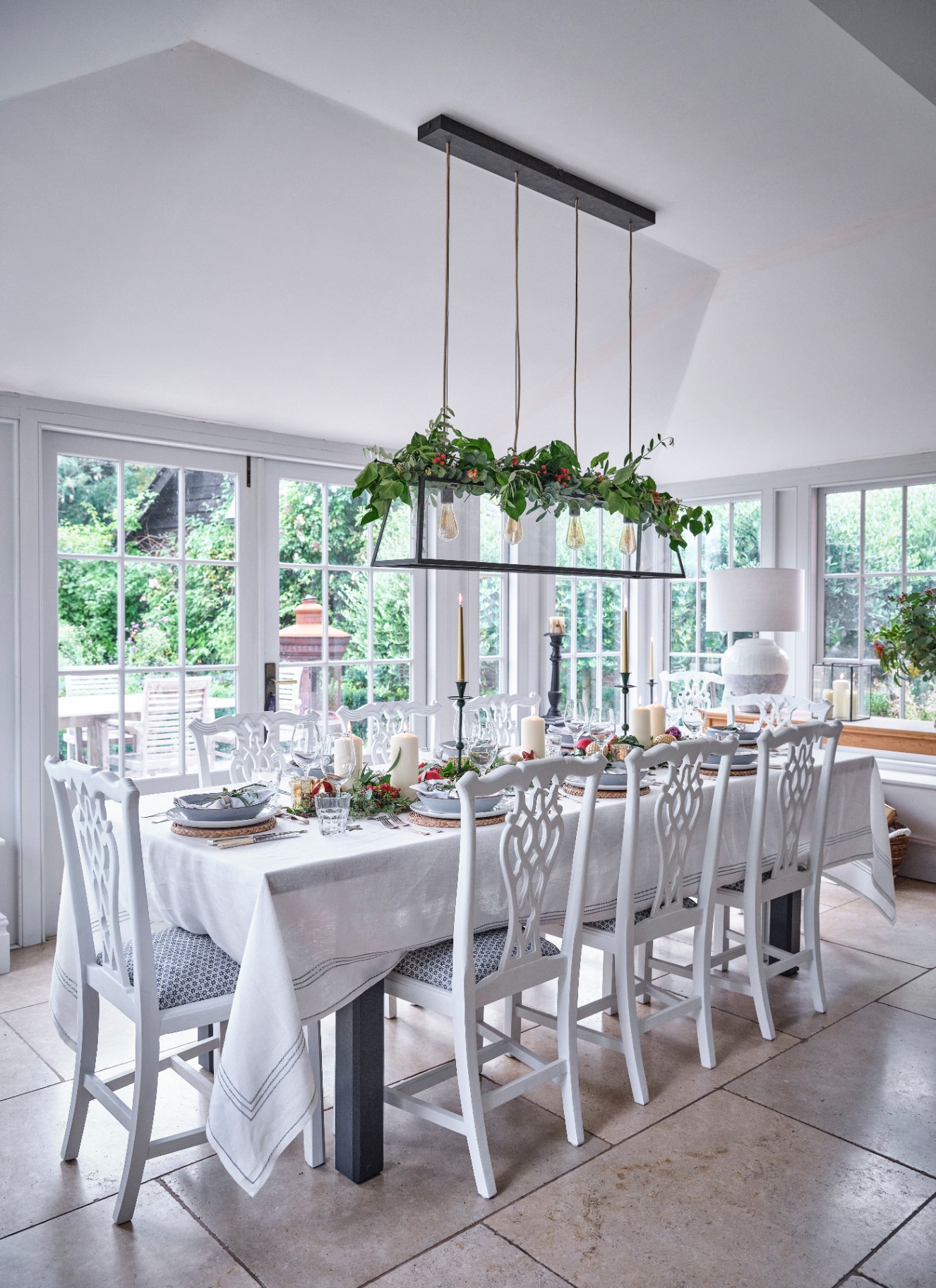 An overhead black pendant light wrapped in lush green foliage above a dining table laid with a white tablecloth