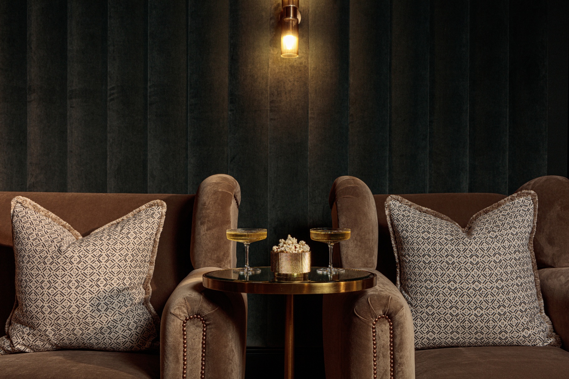 close up of two velvet armchairs with white patterned cushions and a table with popcorn and two champagne coupes