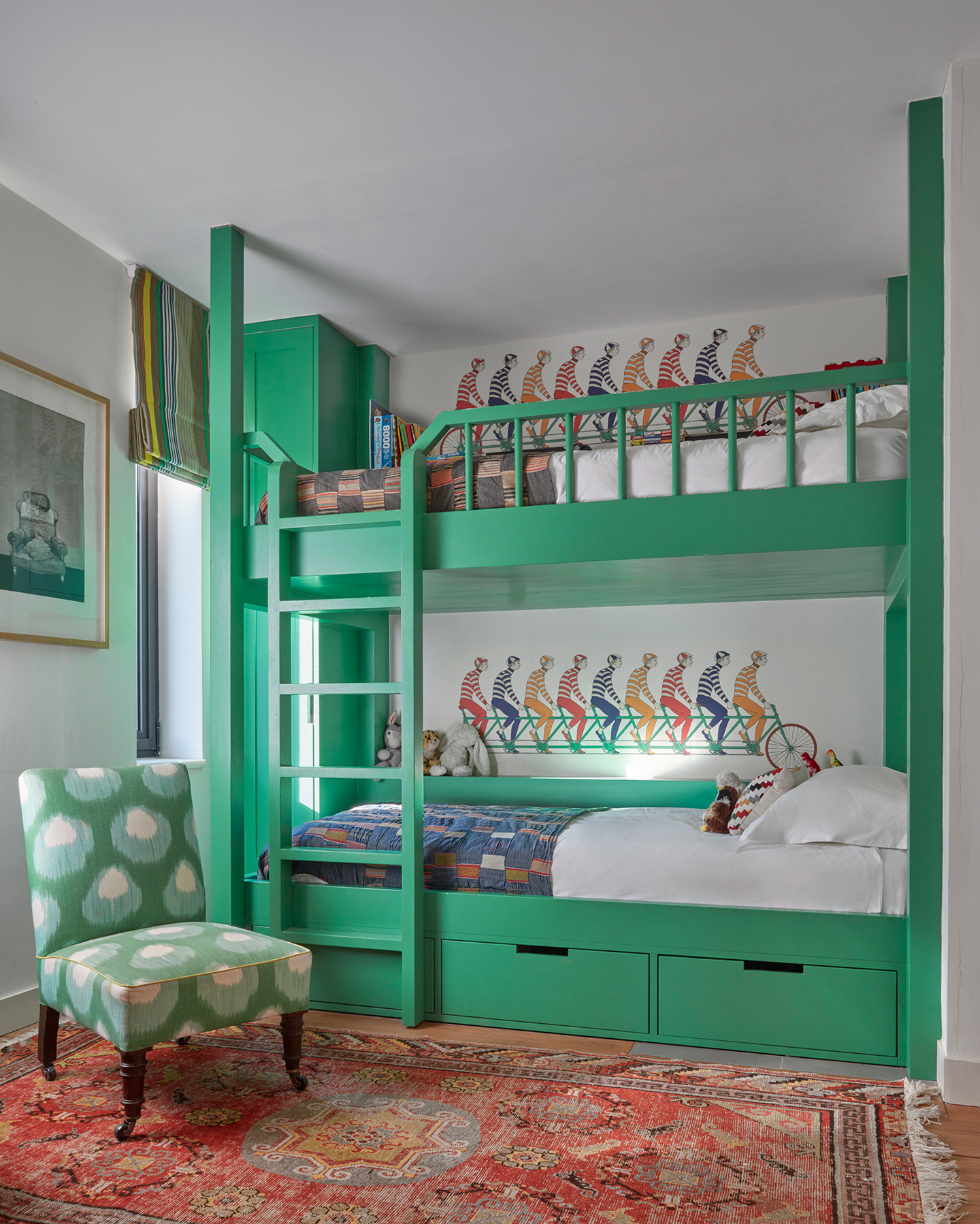 A children’s bedroom with bright green bunk beds and a large traditional-style rug. An accent chair sits to the right. On the back wall behind the beds a wallpaper border with a cycling motif lines the walls