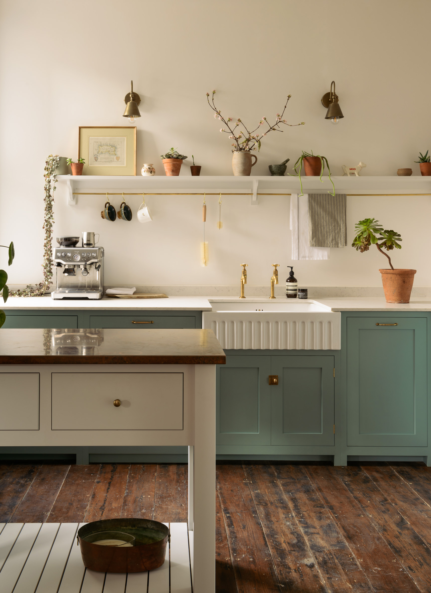 a kitchen with duck egg blue cabinets, wooden floors, a white and wood ktichen island and a belfast sink with a hanging rail and s hooks