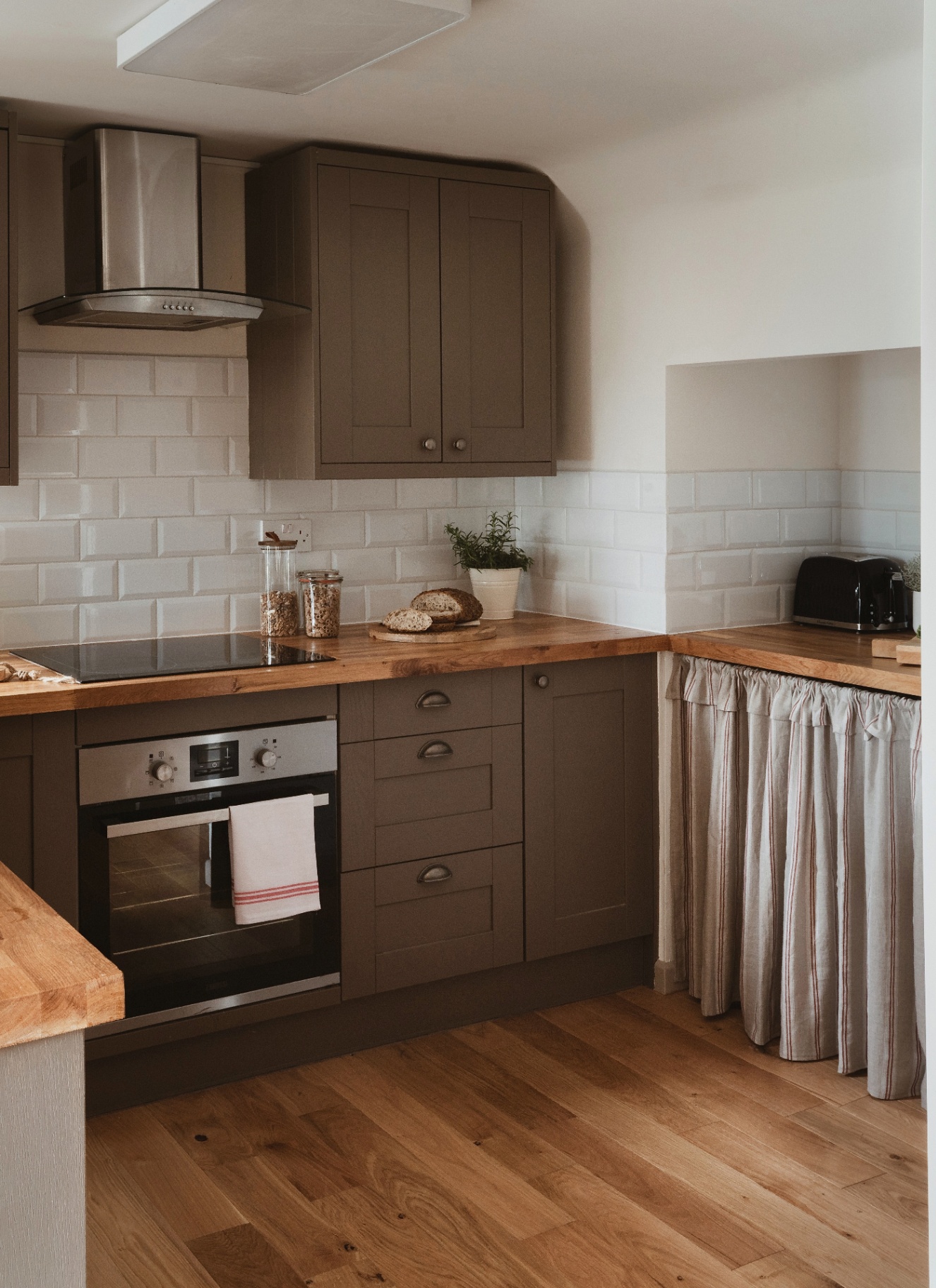 a kitchen with wooden floors, dark green cabinetry and wooden worktops with a grey striped skirt under one of the counters