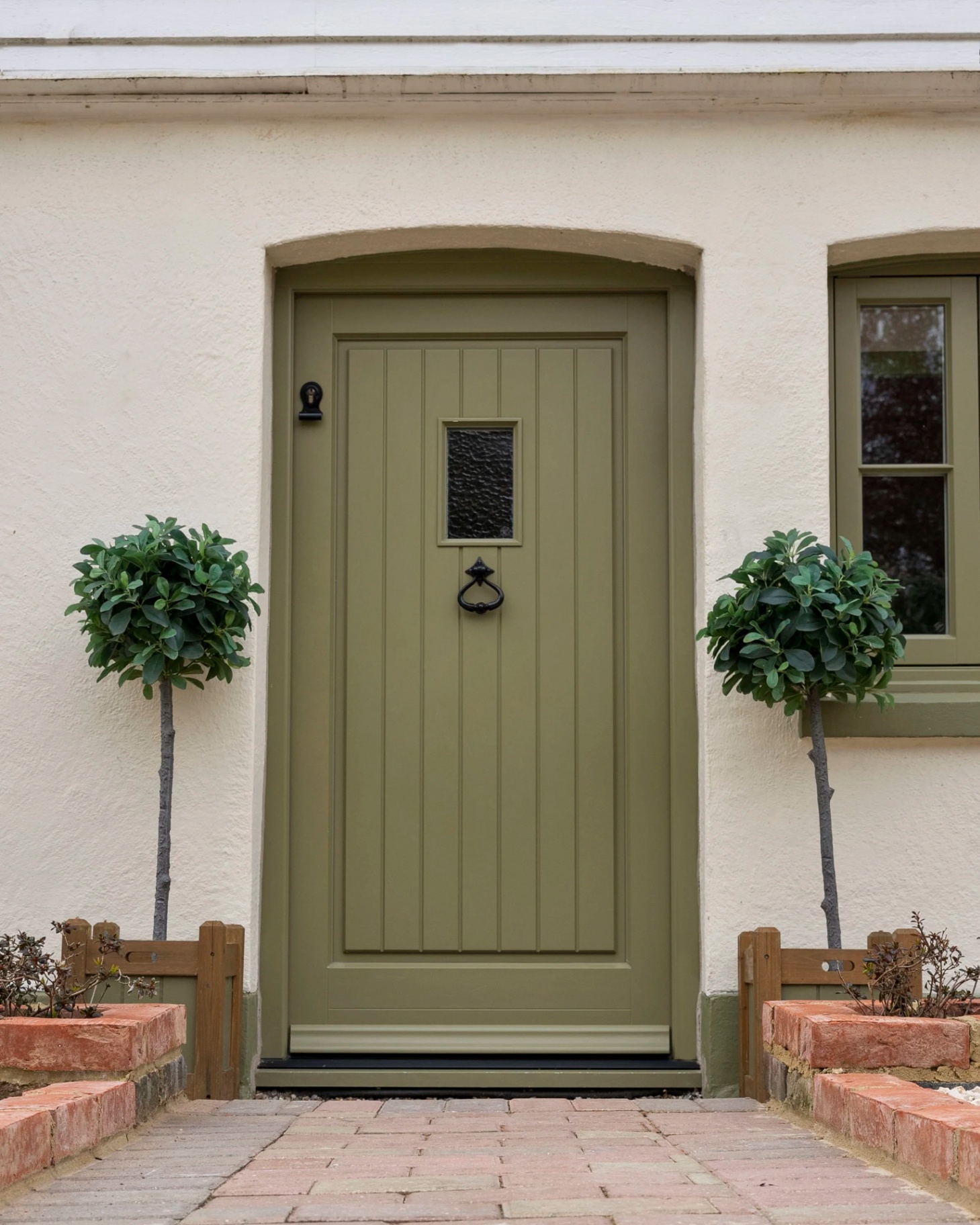 a white house with a green front door and matching window frames and two potted trees either side of the door
