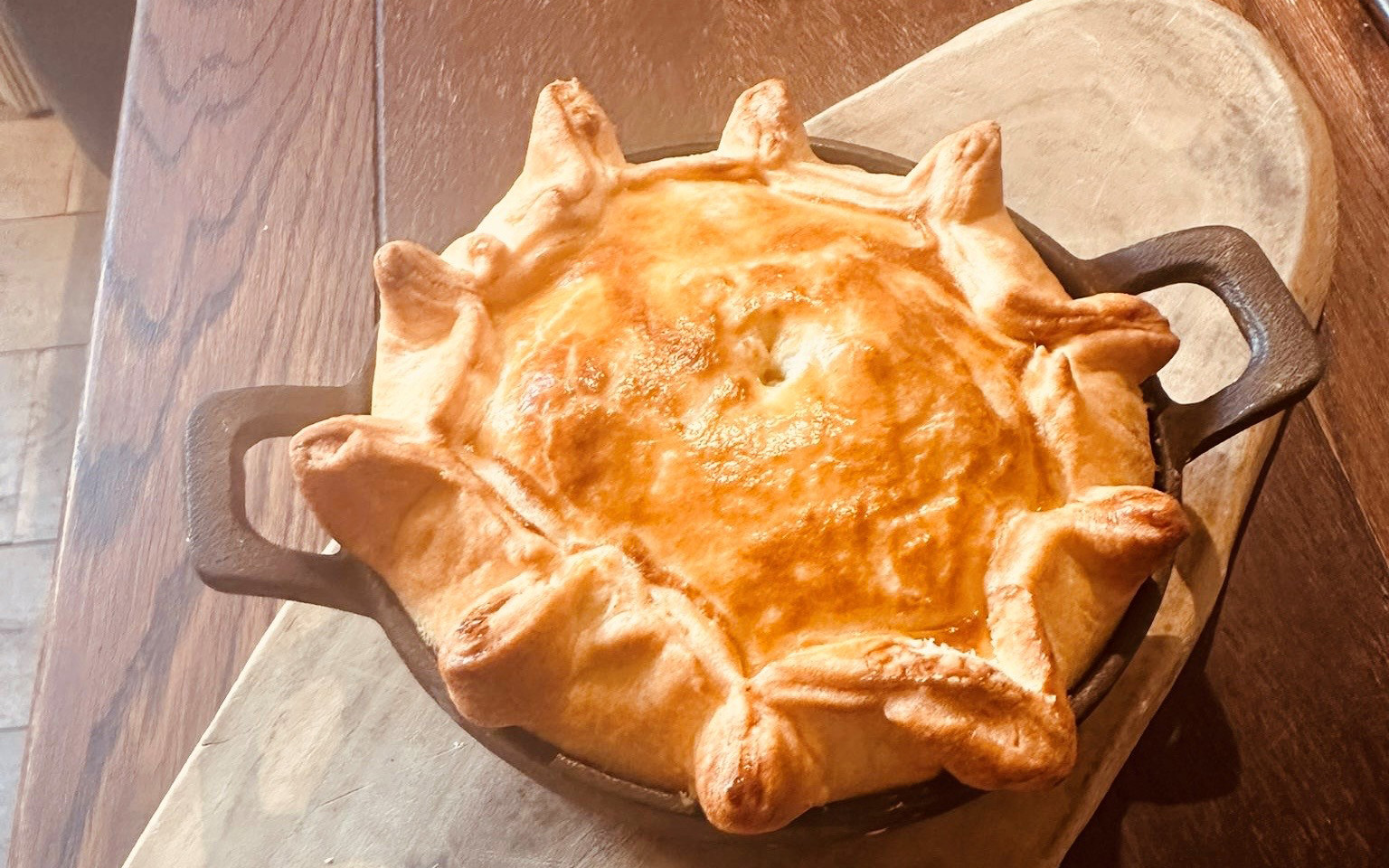 a golden pie in a black pie dish on a wooden table