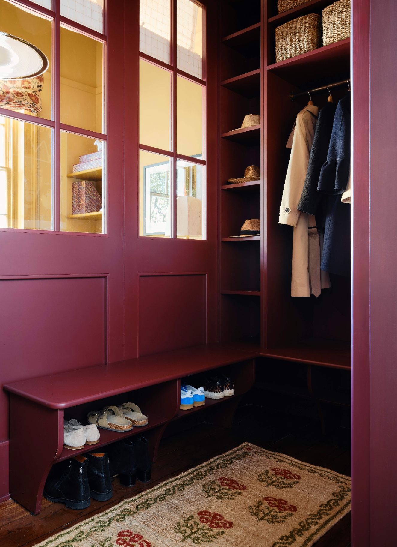 a boot room with burgundy walls and joinery, a jute rug and shelves filled with shoes and coats hung up