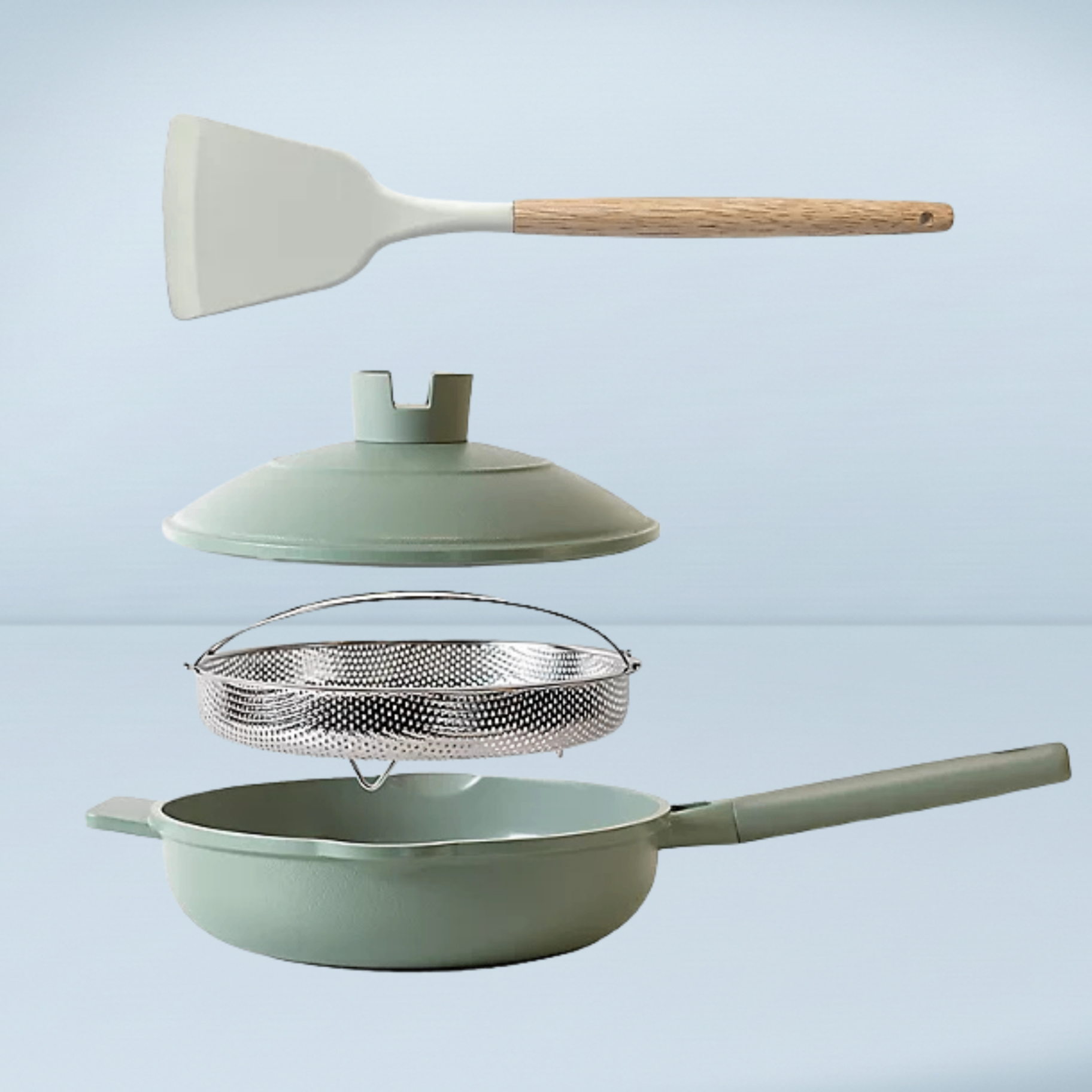 a sage green frying pan with a lid, a steamer basket and a wood and silicone spatula