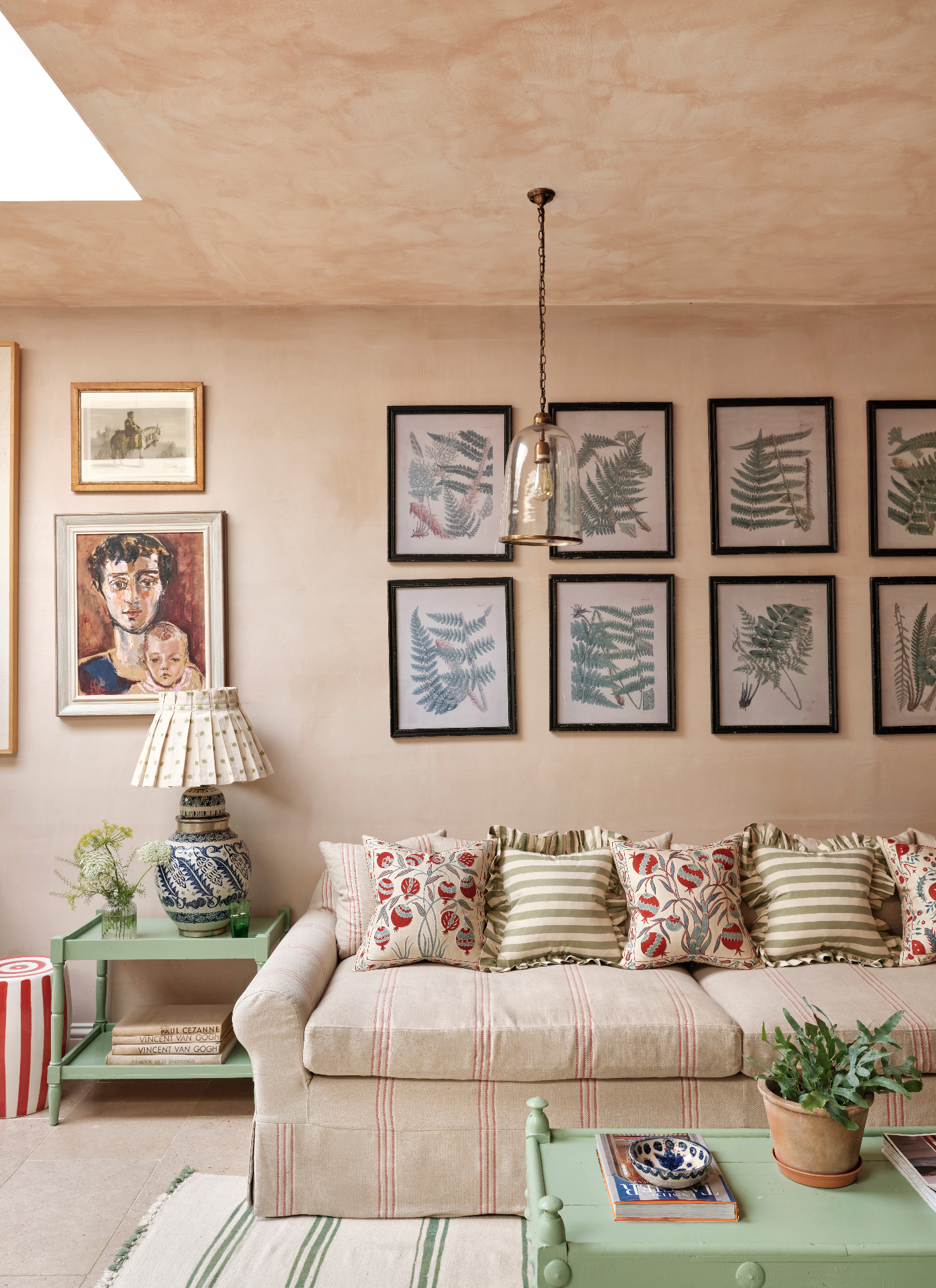 a living room with beige limewashed walls and ceiling, a beige linen sofa with red stripes and a set of botanical prints hanging on the wall