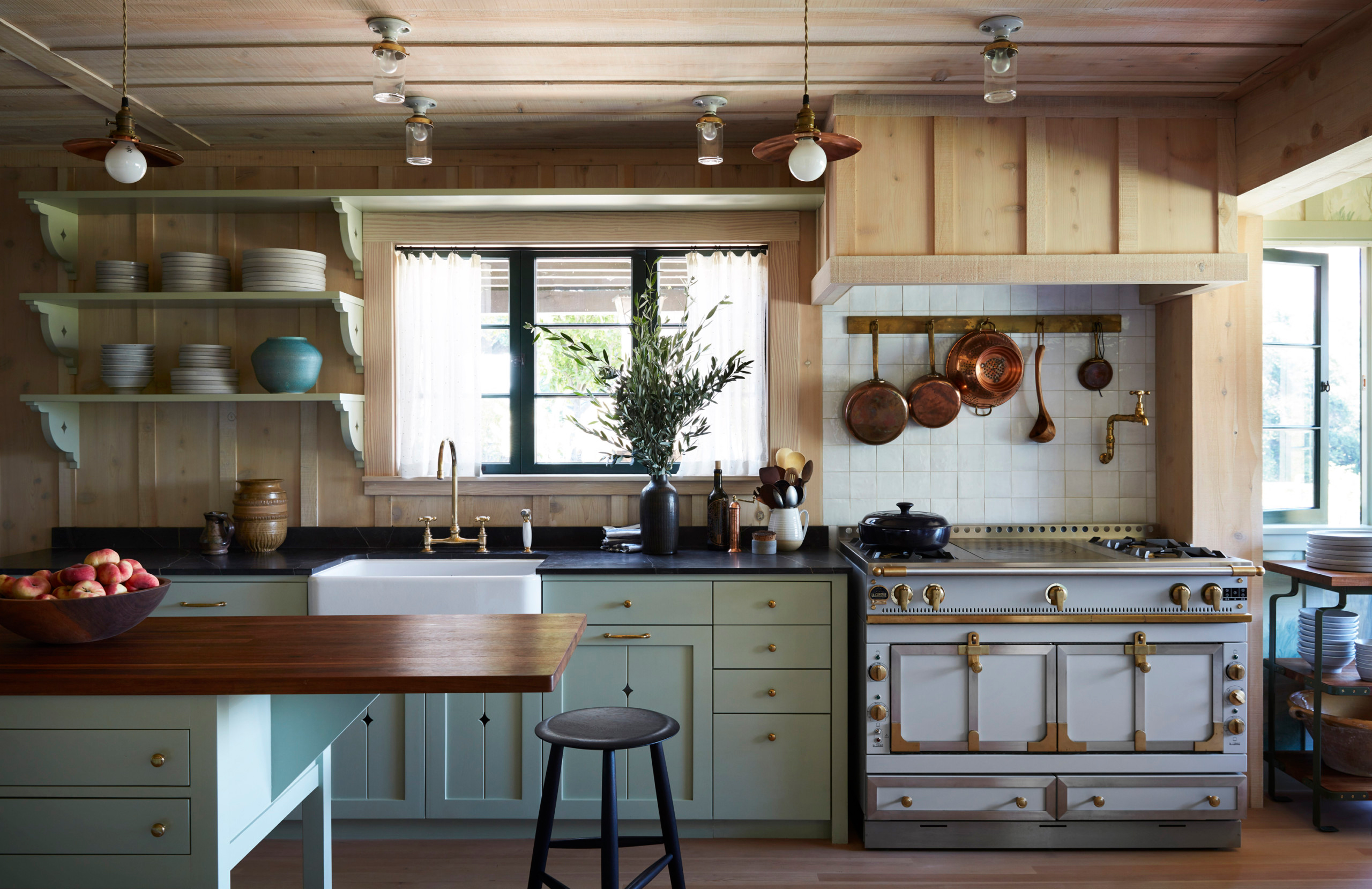 anne hathaway's kitchen with timber walls, a large grey and gol range cooker, copper pots and pans hung above the cooker and duck egg blue painted cabinetry