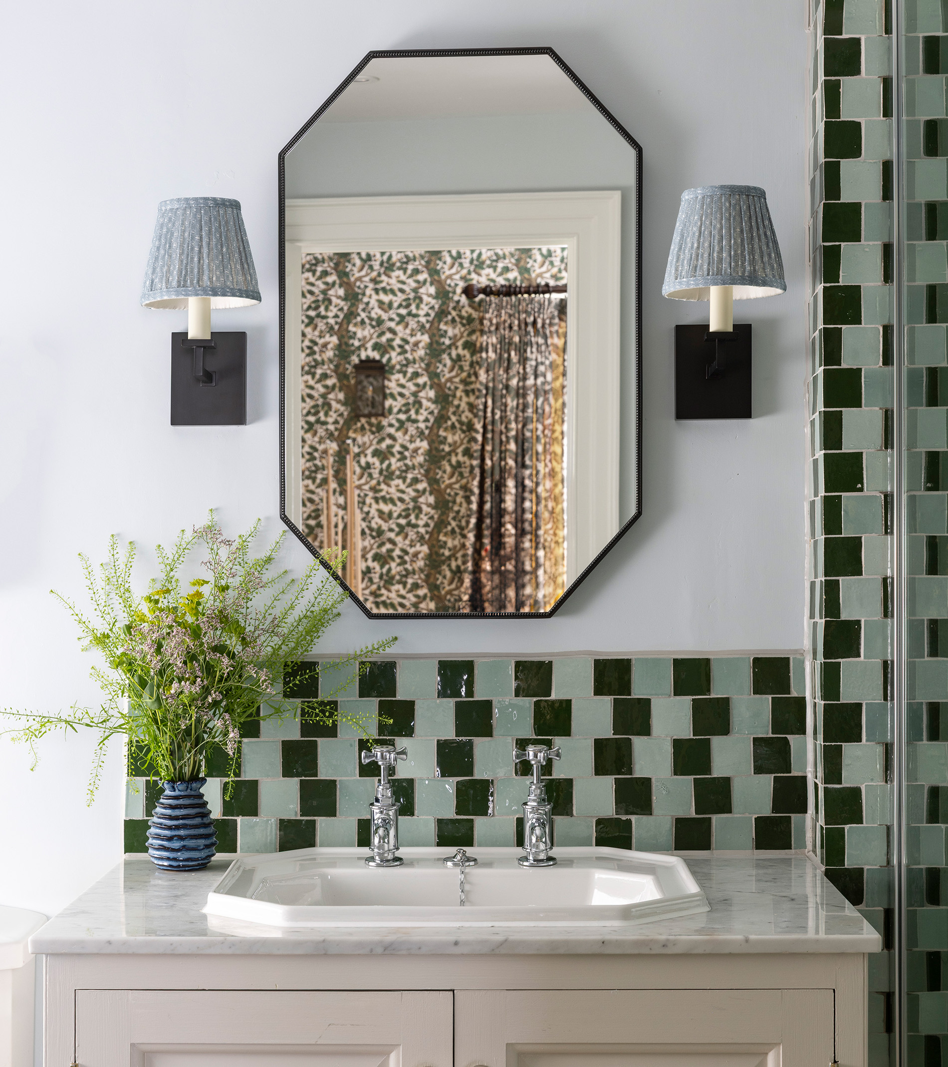 a bathroom mirror with two blue pleated wall lights either side, green checkerboard tiles and a sink