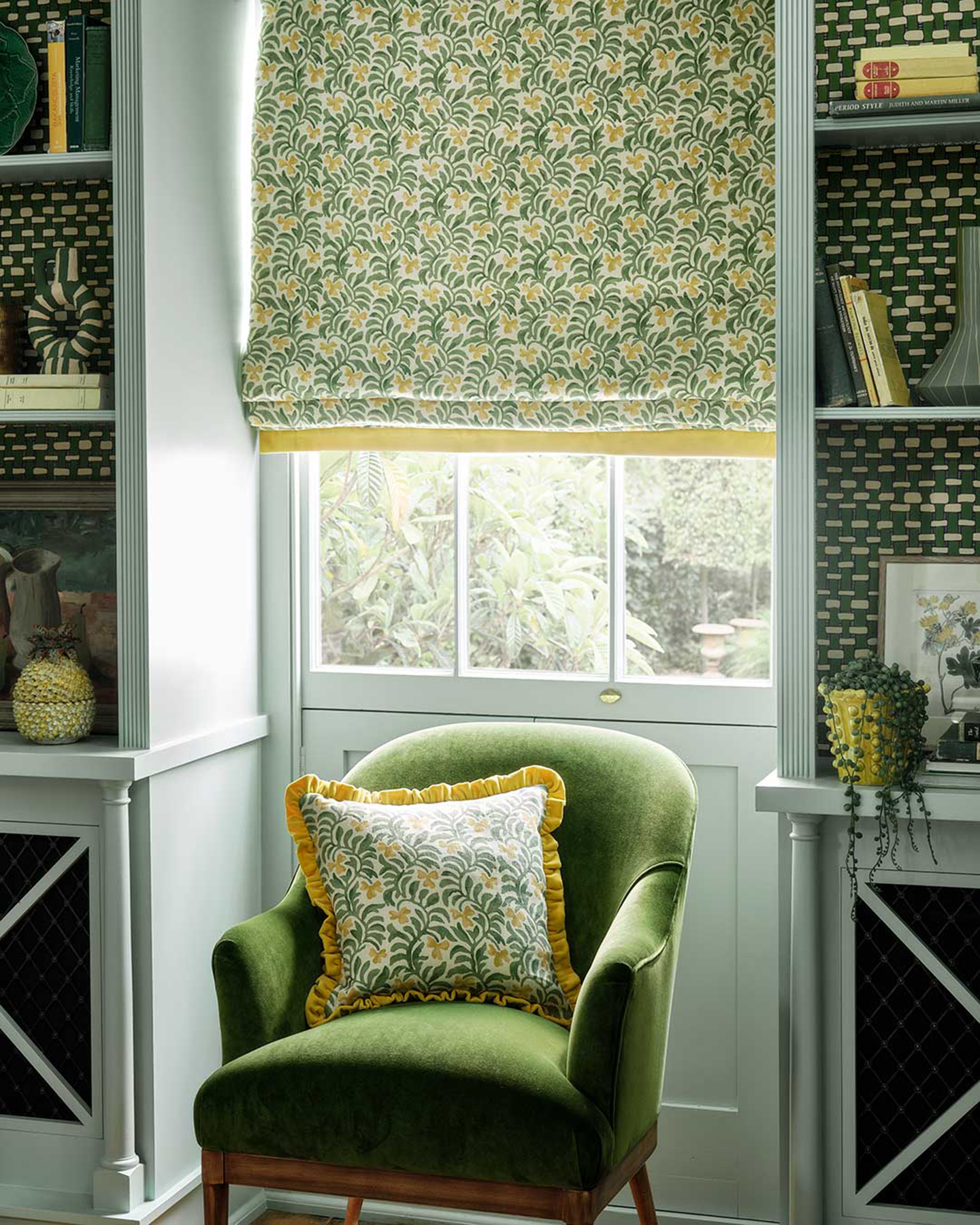 a reading nook with a green velvet armchair in front of a window with a green botanical patterned fabric blind