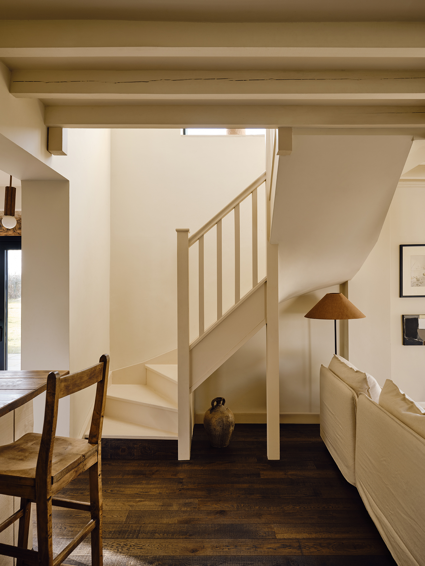 A curved white stairwell situated between a sofa and a kitchen island with a bar stool. 