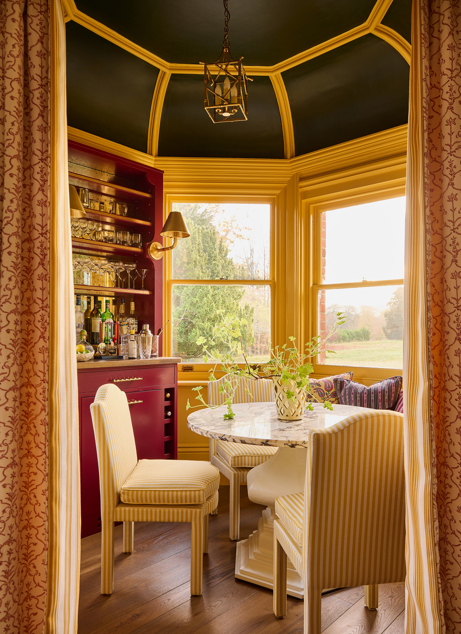 a circular bar area with a black and yellow painted ceiling, a round table with yellow and white striped chairs and a red painted bar wtih glasses and drinks